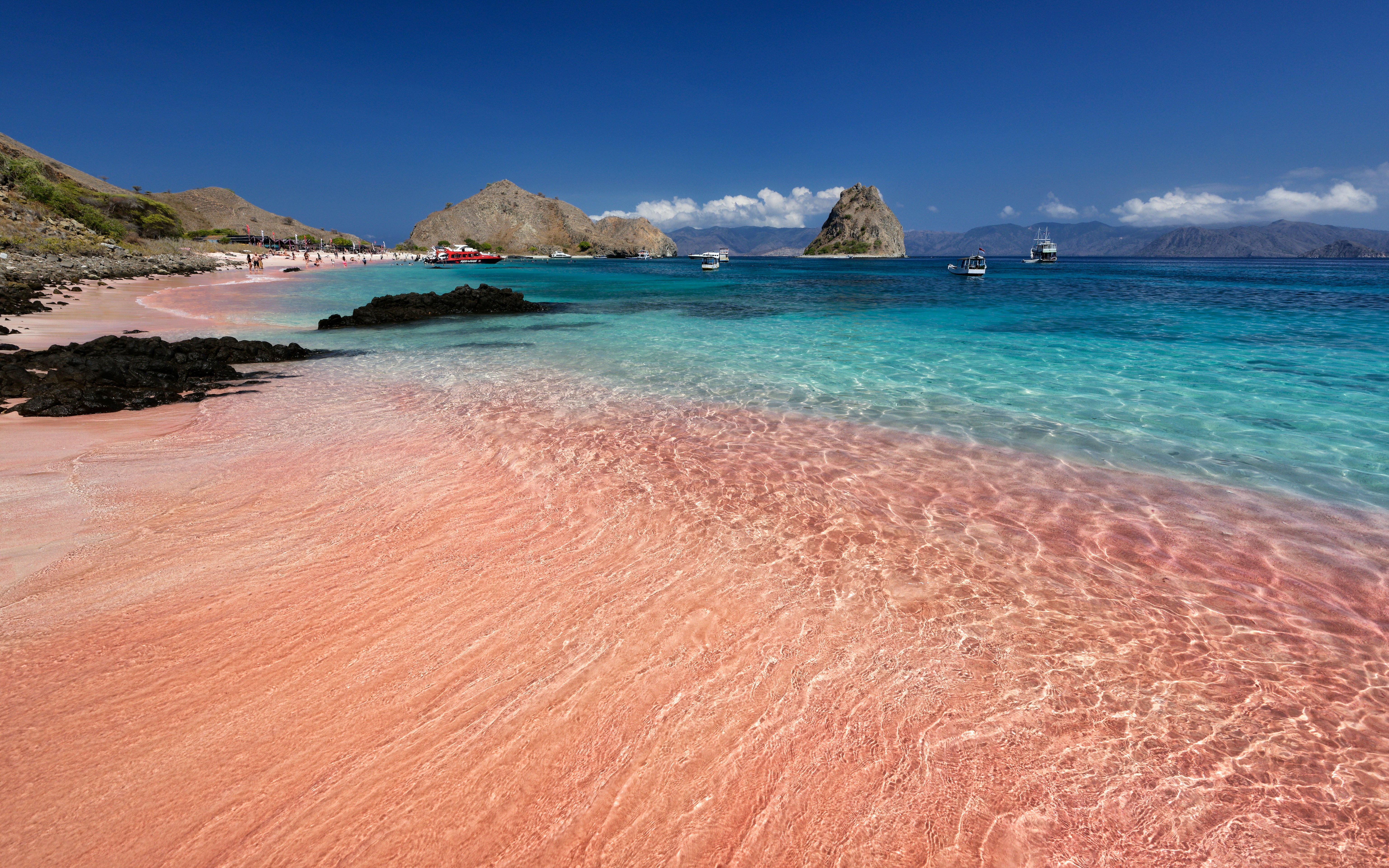 A sandy beach with clear blue water and pink sand