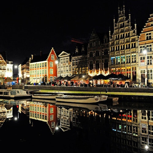 夜晚的城市景观中，历史建筑灯火辉煌，映照在平静的运河中，船只停靠在水边。