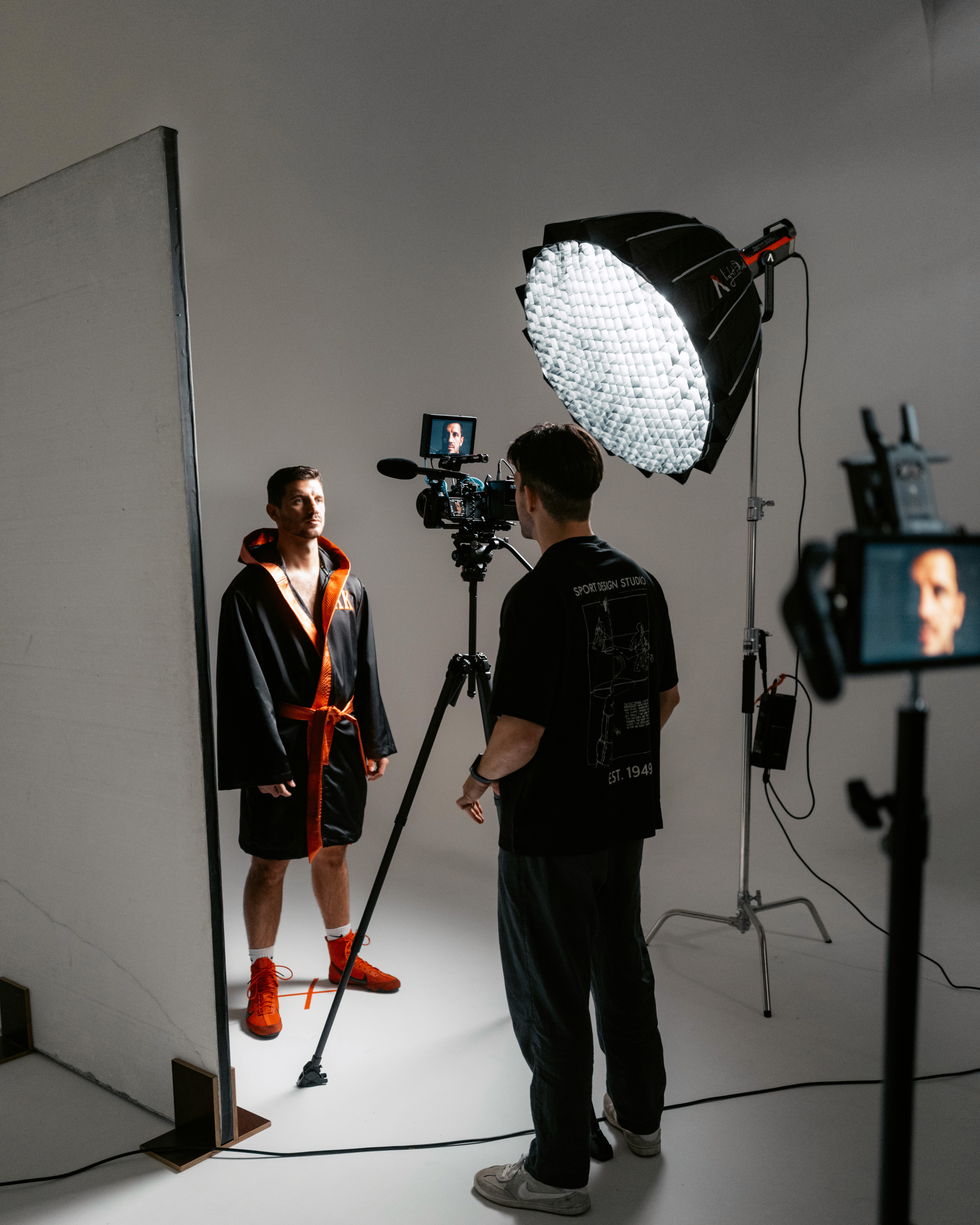 Fotoshooting im Studio: eine Person steht vor der Kamera, während ein Fotograf mit professioneller Beleuchtung und Monitor arbeitet.