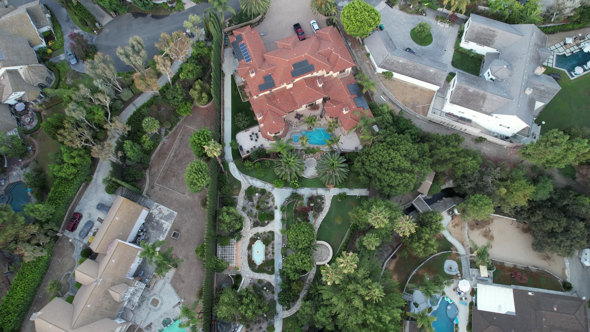 Overhead view of a red-roofed home, swimming pool and garden paths around planted areas.
