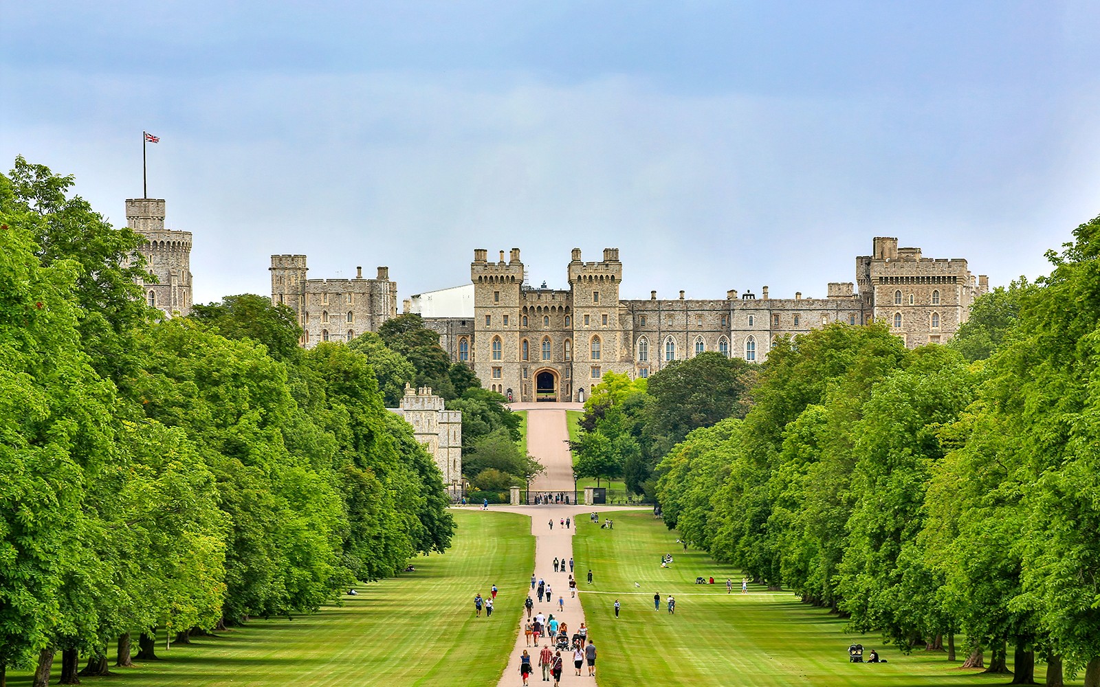 Tourists walking towards Windsor Castle through a tree-lined path on a day trip from London.