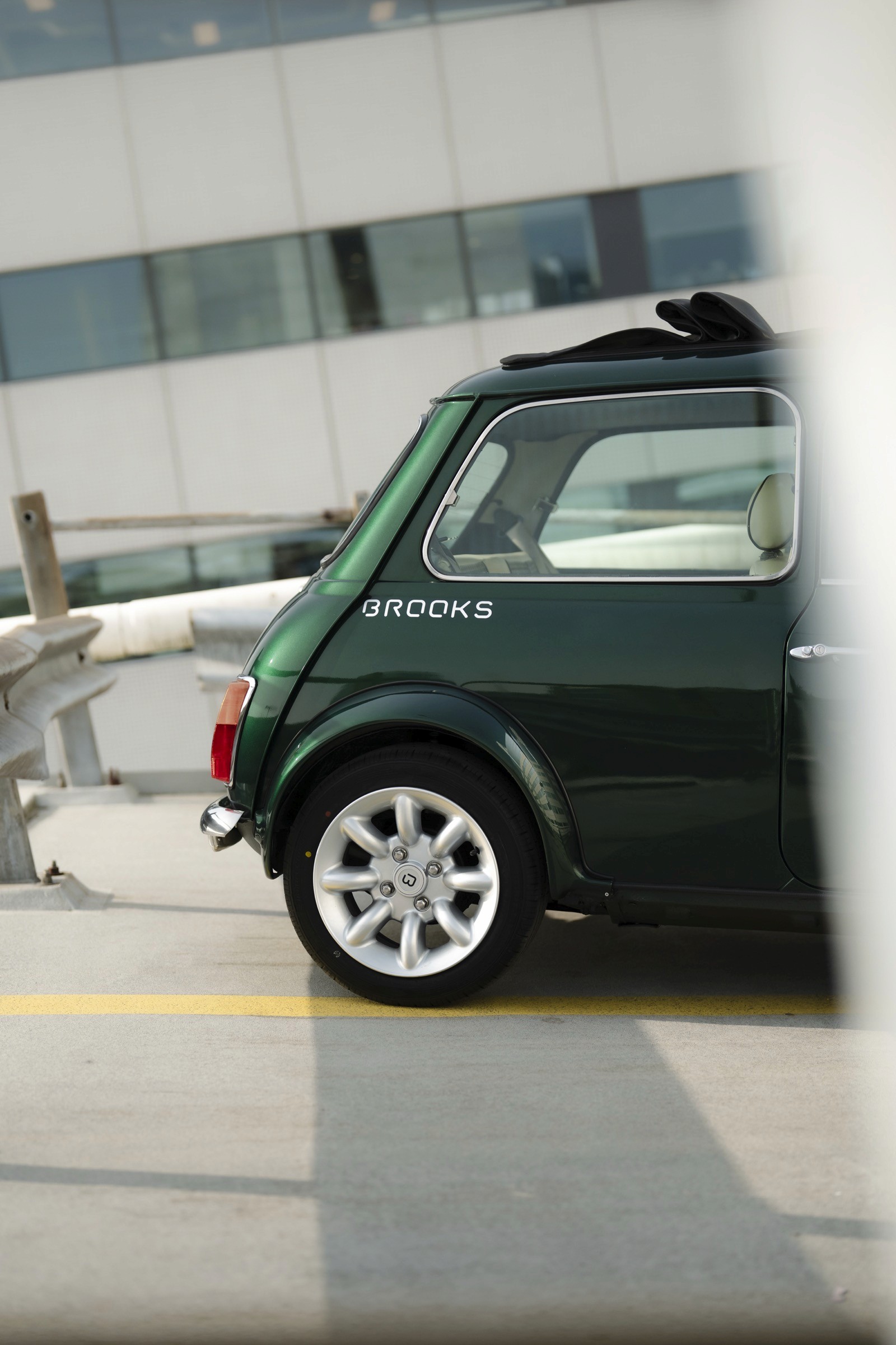 A close-up view of a green car parked beside a modern building, showcasing its wheel and side profile.