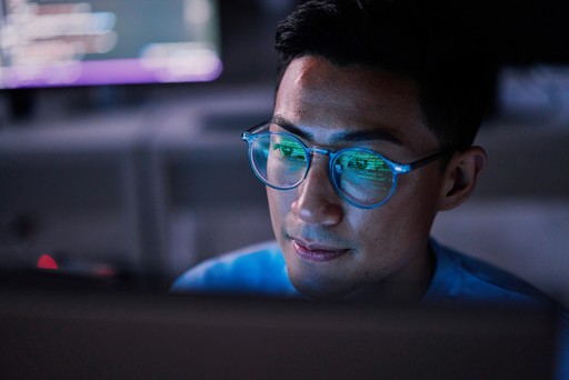 man working on a computer with the reflection of his screen in his glasses