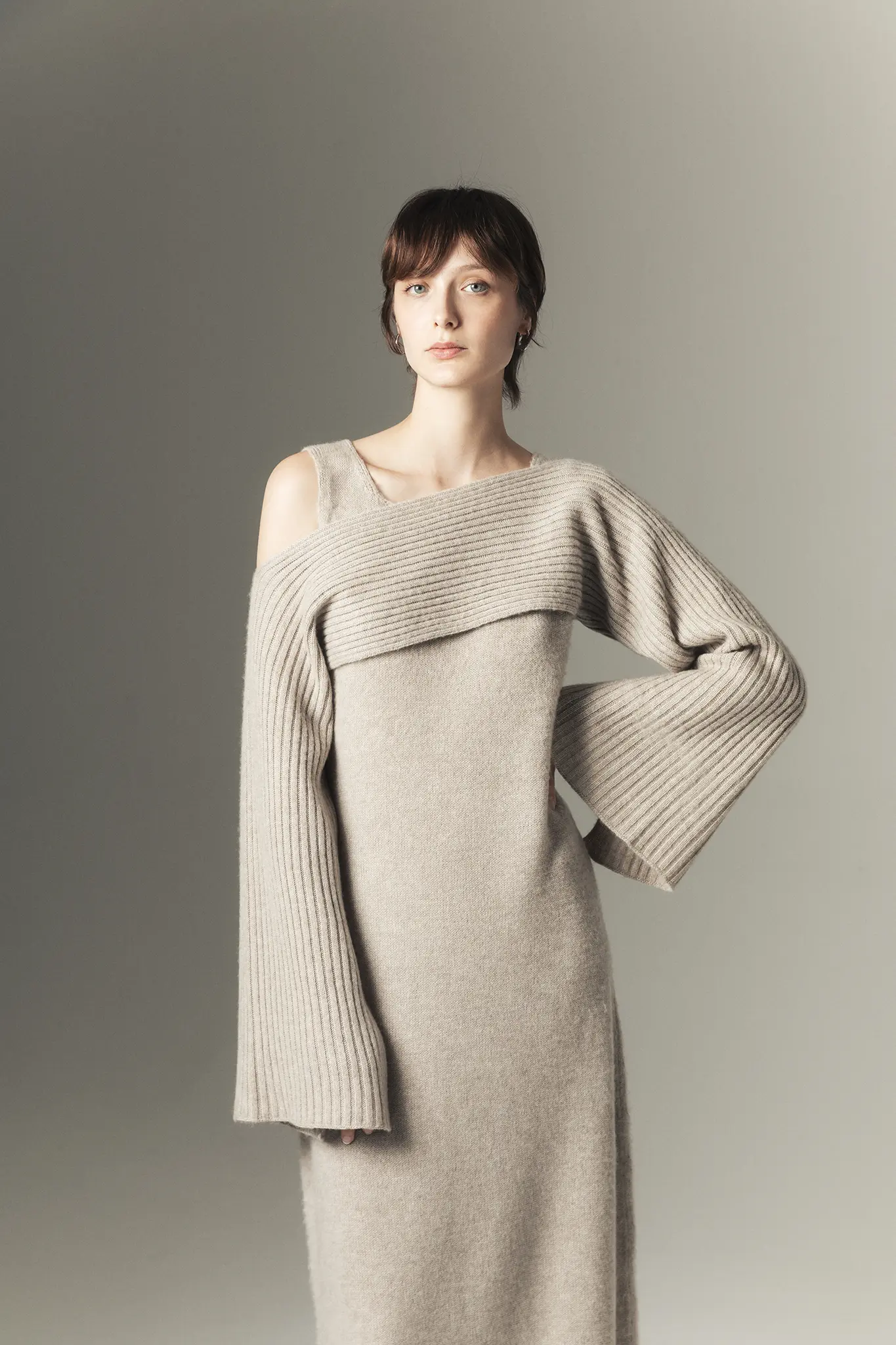 Woman wearing taupe one-shoulder cashmere dress with ribbed long sleeve and asymmetrical neckline – Aida Barni Fall Winter 25/26 collection.