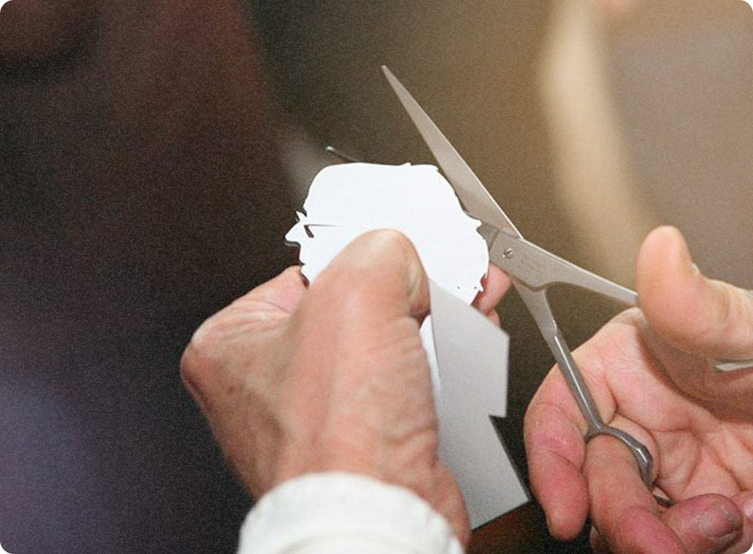 Un silhouettiste découpe minutieusement une forme en papier avec des ciseaux, concentré sur son travail.