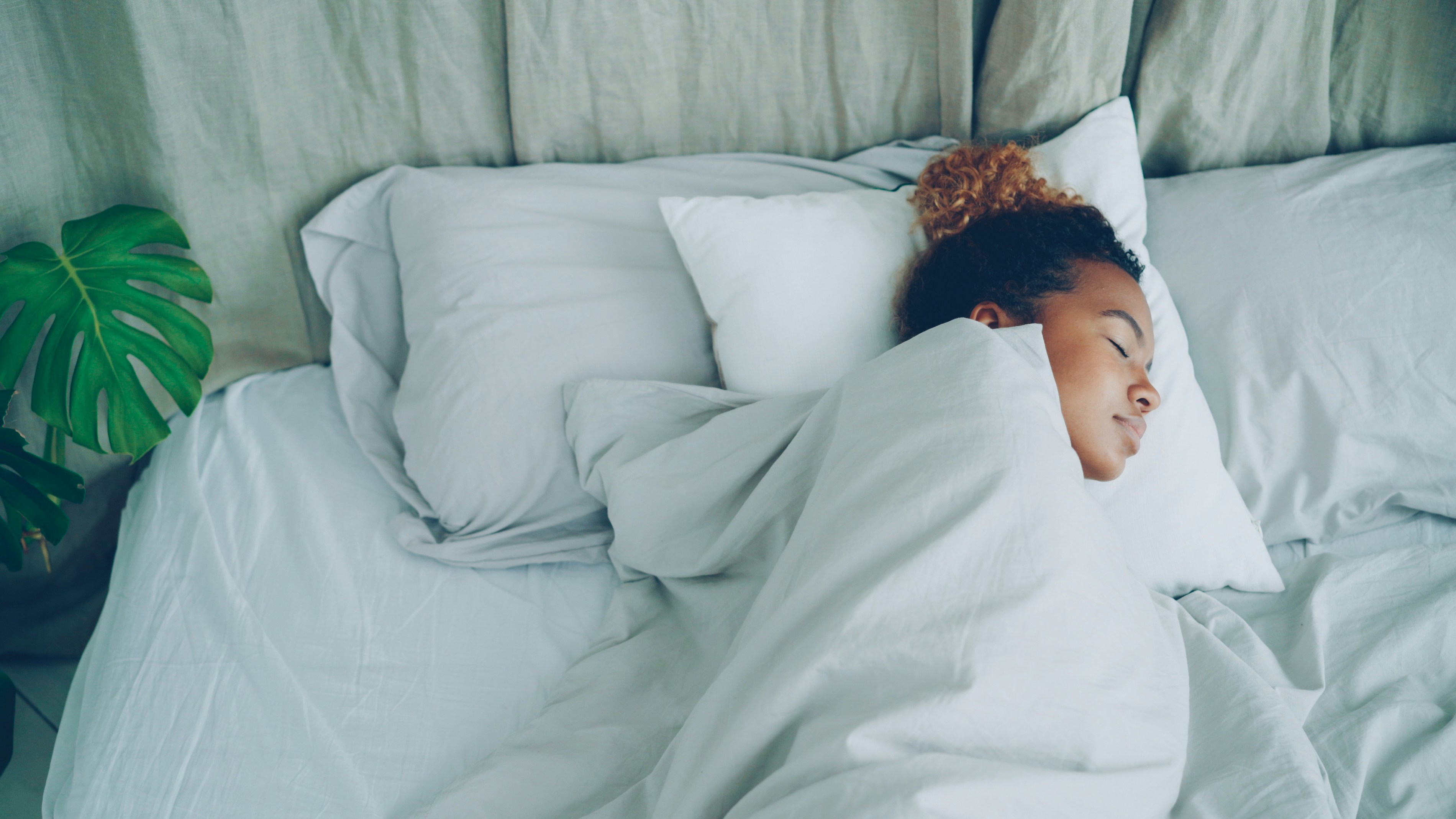 A young woman sleeping peacefully in a white bed.