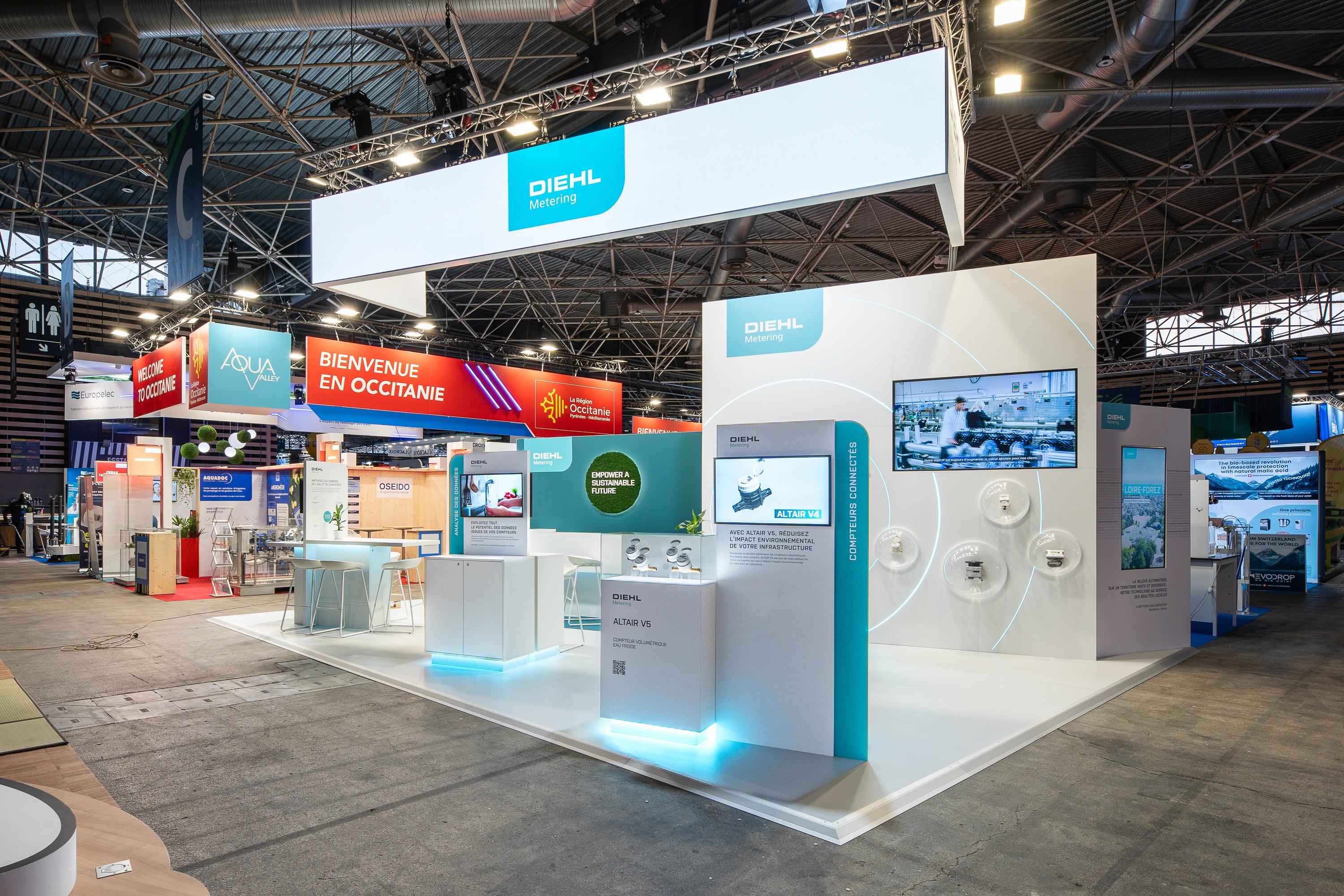 Stand Diehl Metering Pollutec 2025 par Expace – détail de l'espace lounge avec décor mural turquoise, logo végétal en mousse stabilisée et mobilier design blanc et bleu