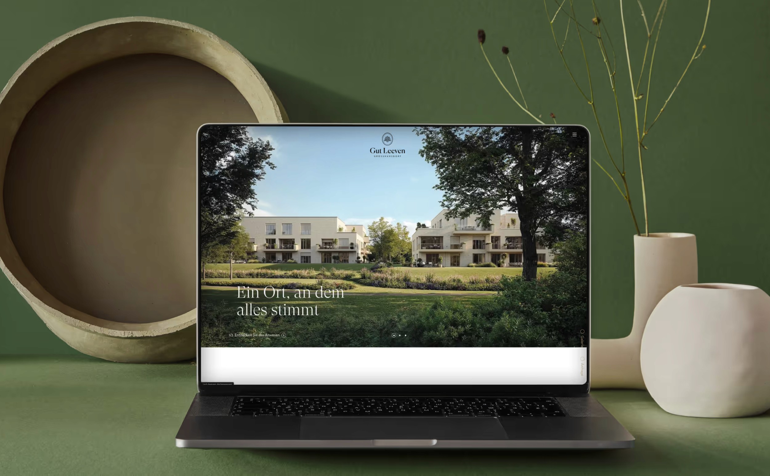 MacBook-Mockup zeigt die Startseite der Gut Leeven Immobilien-Website mit dem Claim "Ein Ort, an dem alles stimmt" und einer atmosphärischen Architektur-Visualisierung.