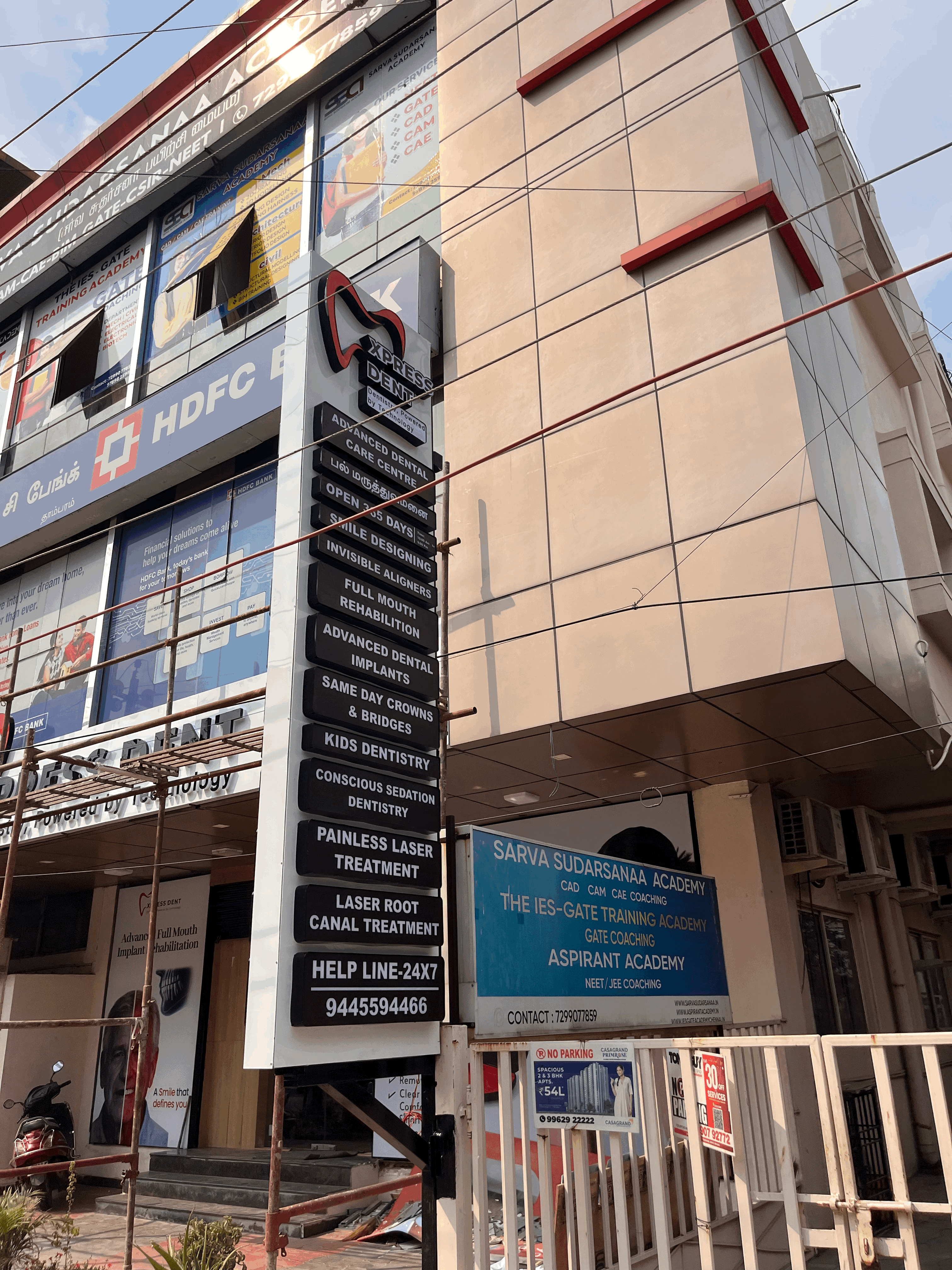 A man in a blue bomber jacket stands against a dark background. The lighting is dramatic, highlighting his focused expression. His pose is confident.