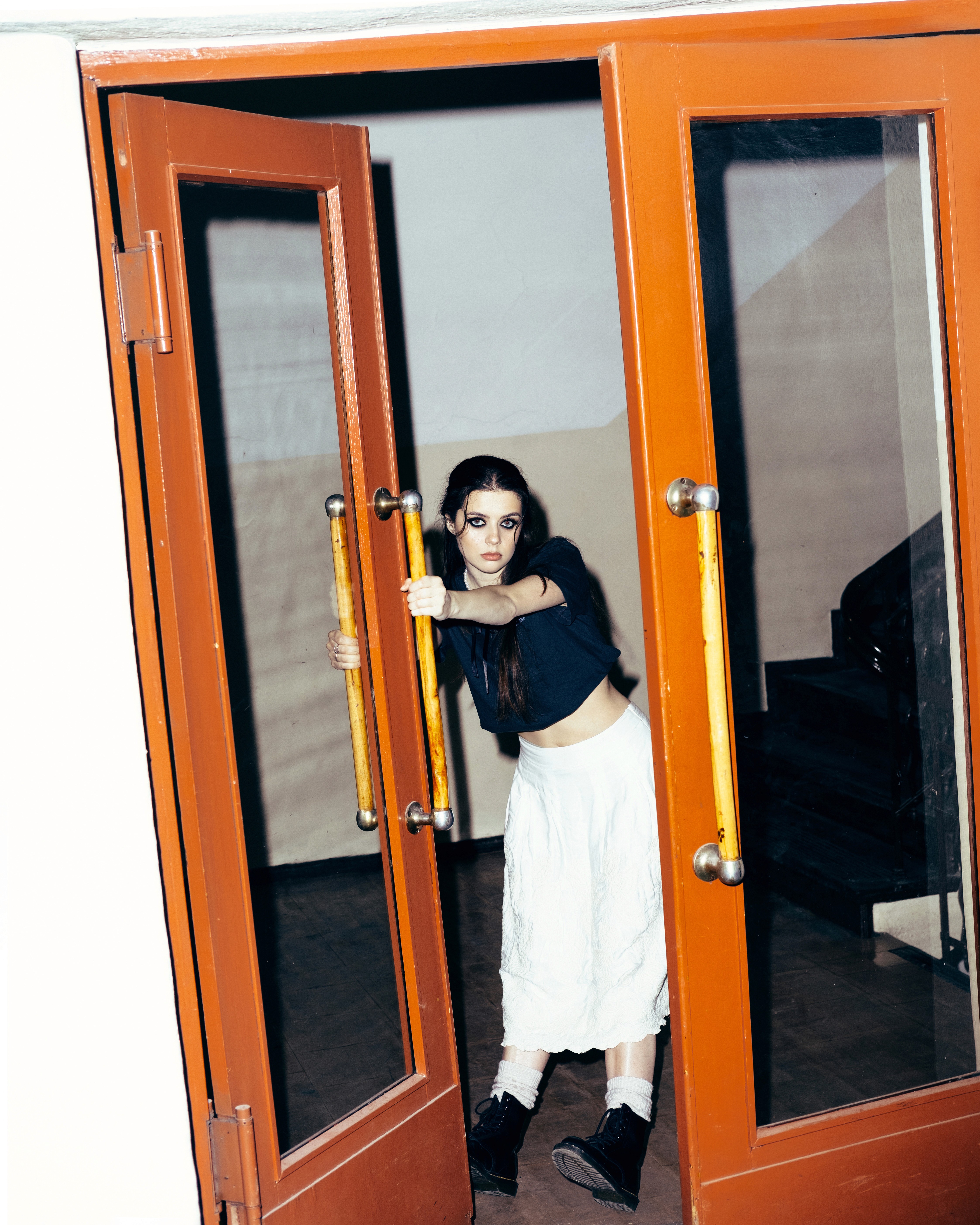 Tanya – Youth Disorder – pulling open double orange doors while staring directly forward