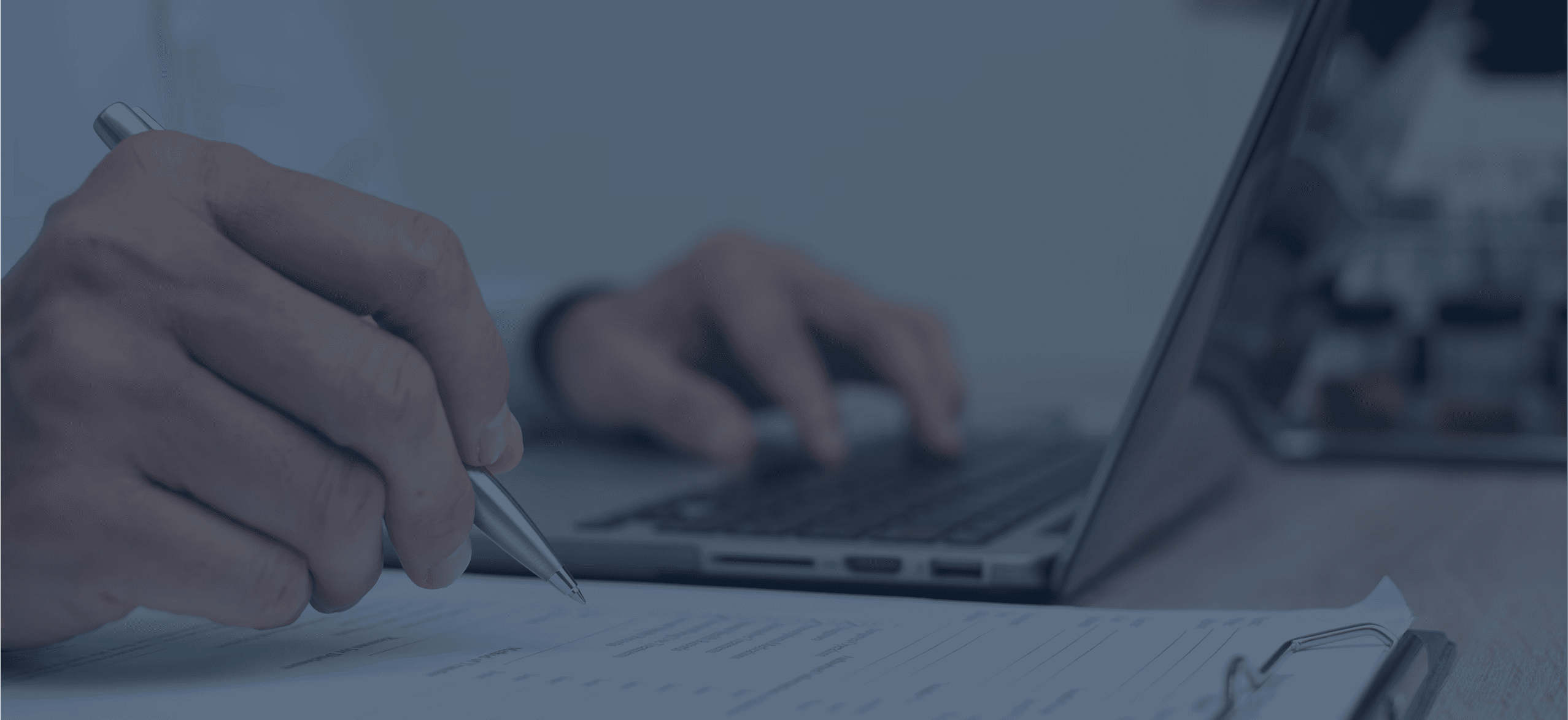 Close-up of a person's hands, using a pen, paper and a laptop.