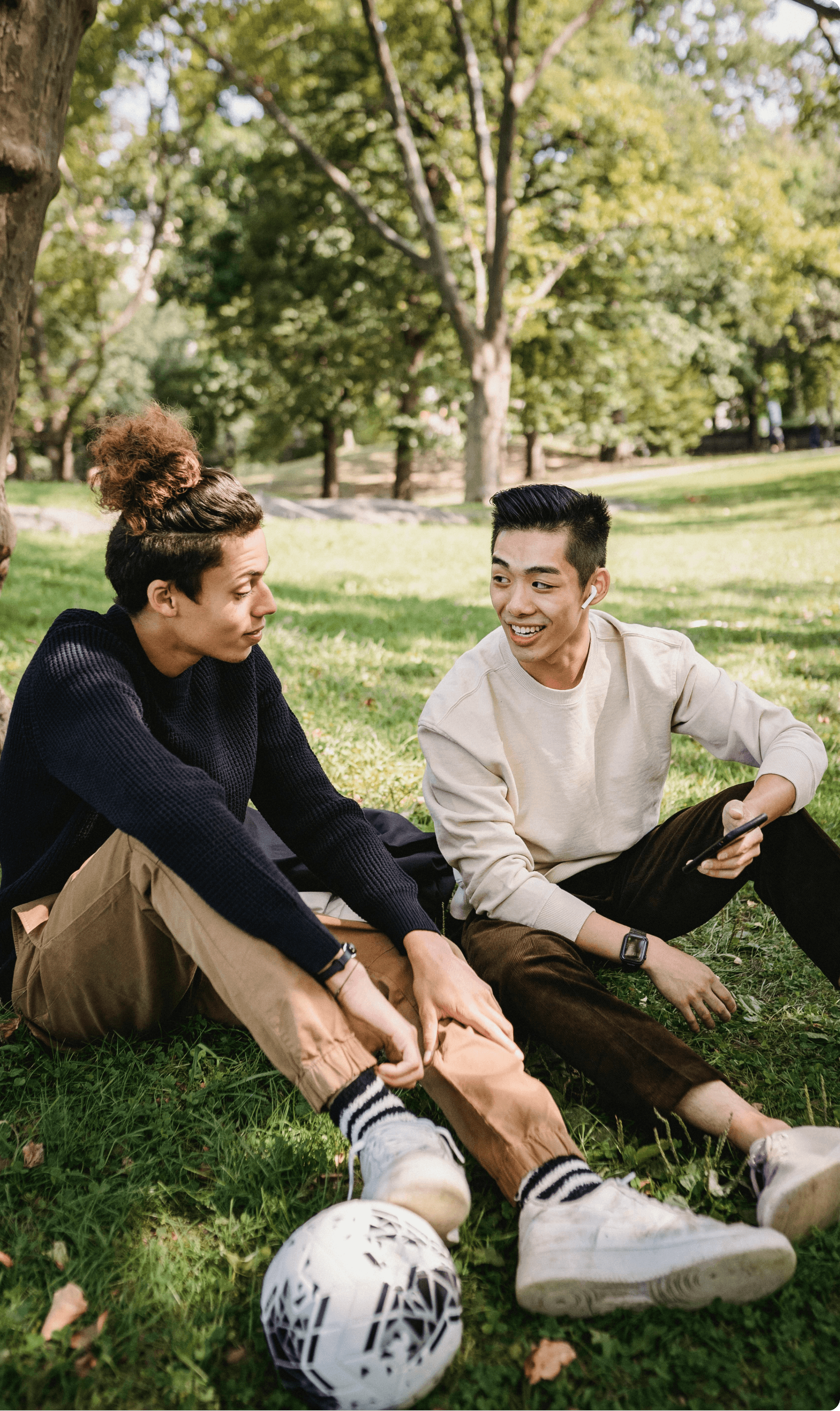 Two adult friends chatting in the park while sitting on the grass