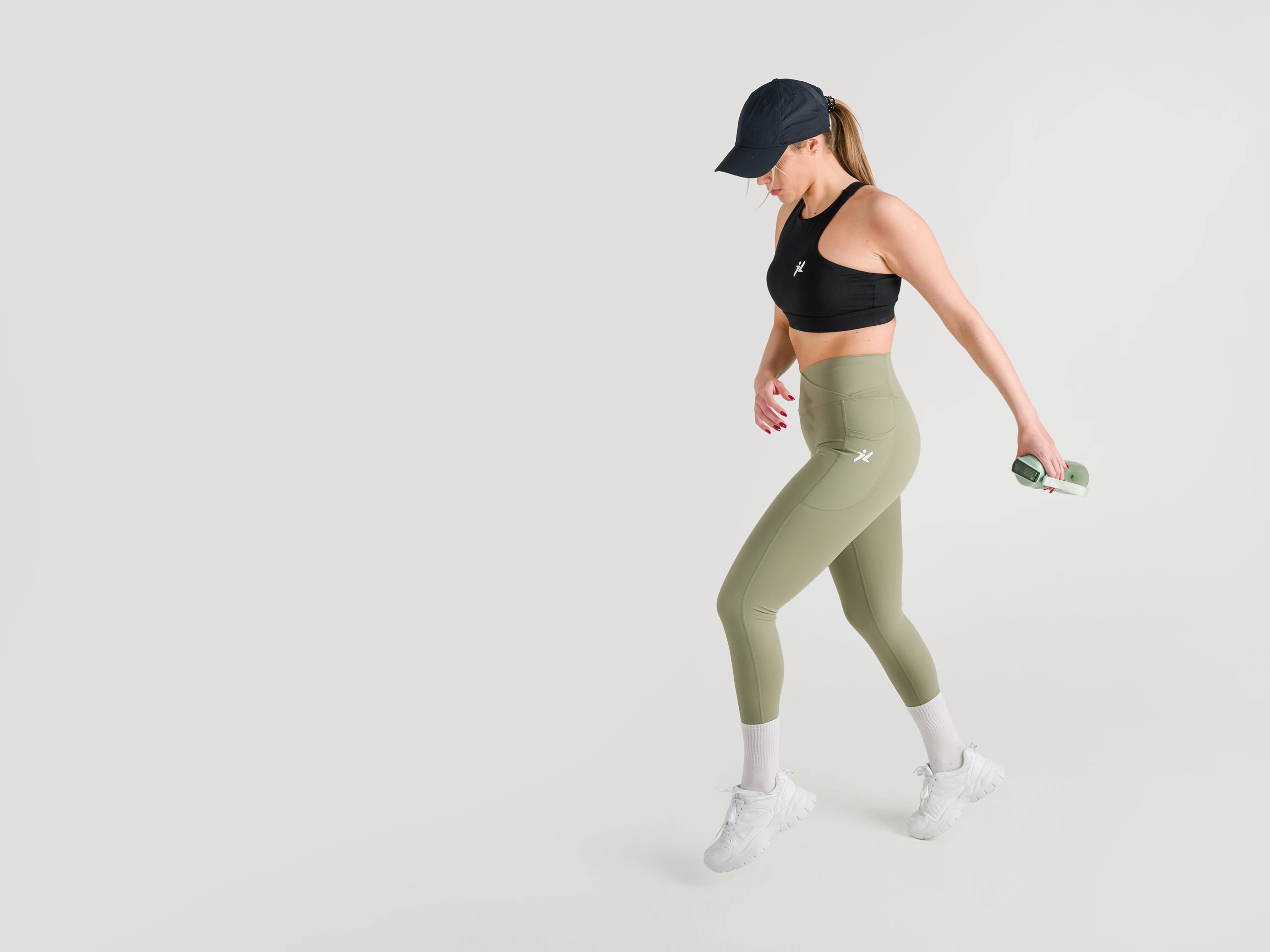 Female athlete in green leggings and a black sports bra, holding bottle in a studio.