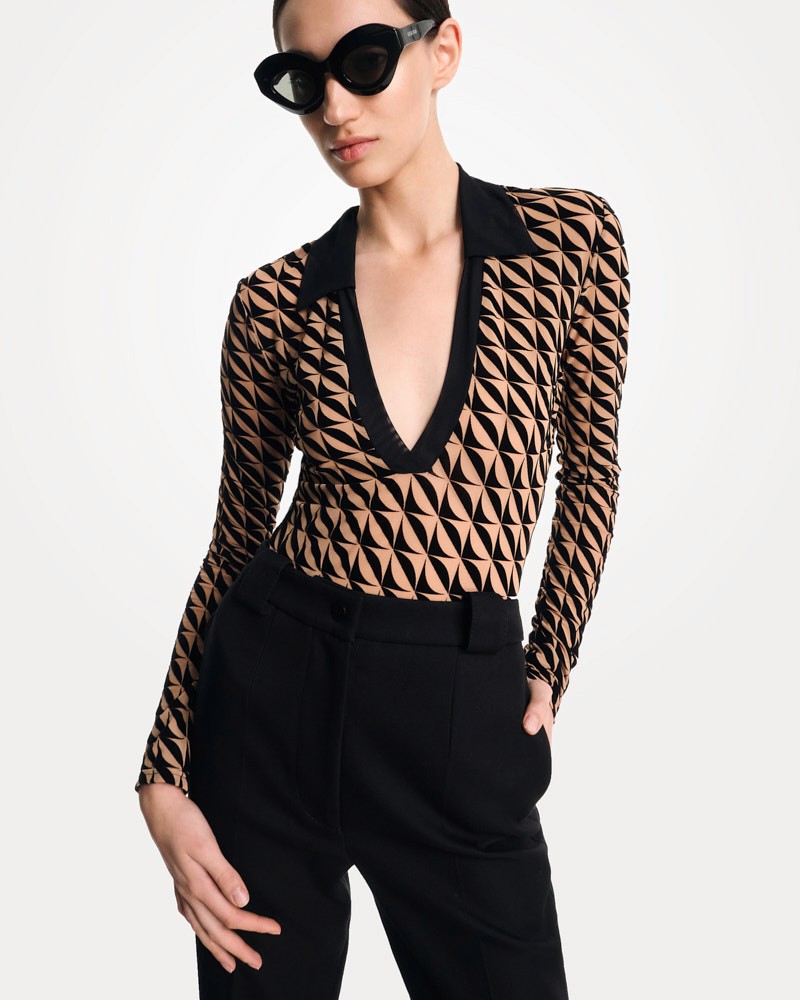 Fashion model wearing geometric bodysuit, black trousers, and sunglasses in studio campaign photography.