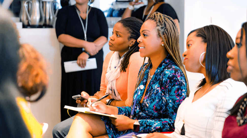 A smiling young man with crossed arms, wearing a plaid shirt and white t-shirt, poses against a dark background.