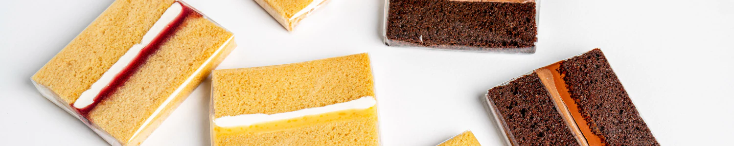 Close-up view of various cake slices showing different flavors and fillings, including vanilla cake with cream filling and chocolate cake with caramel filling, arranged on a white background.