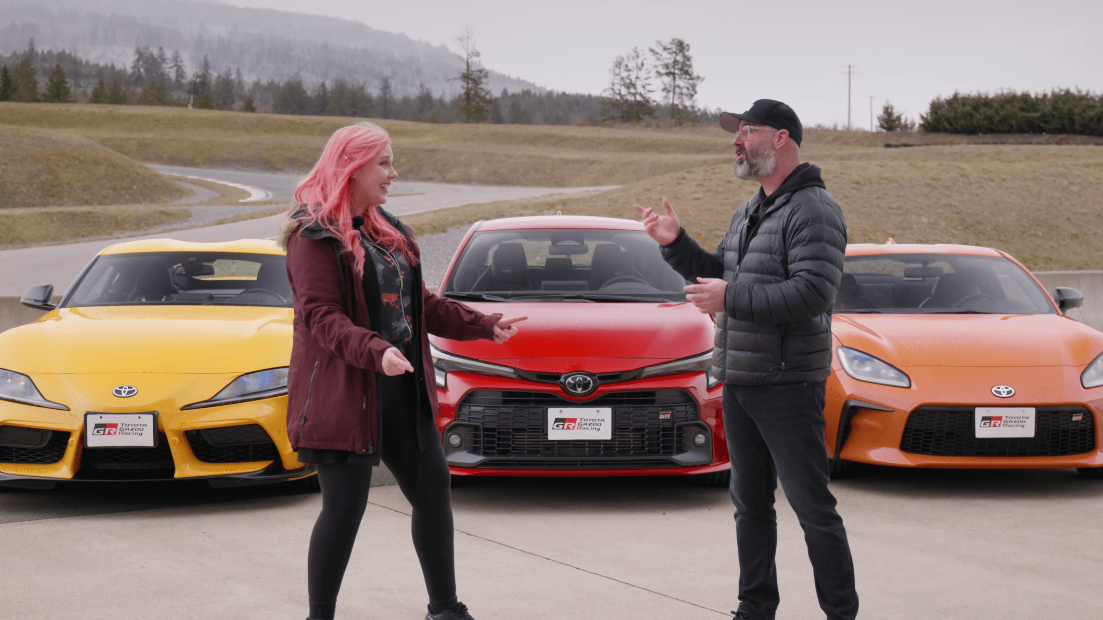 MissHarvey and a host talk in front of a GR Supra, GR Corolla and GR86 at the track