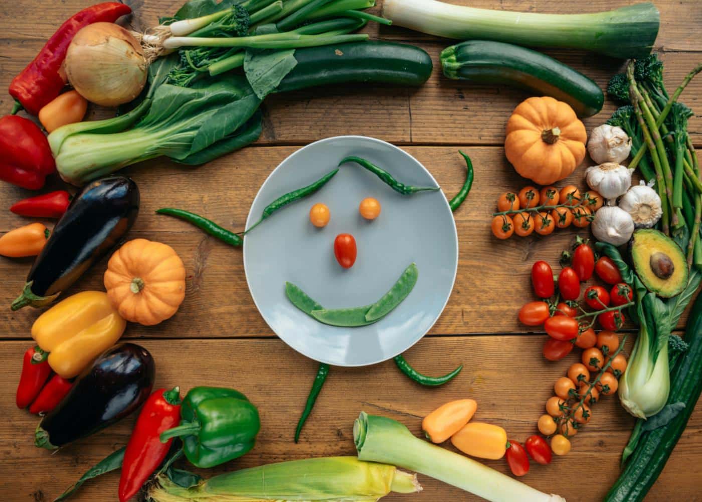 Vegetables surrounding a round plate with veggies on it to make a smiling face