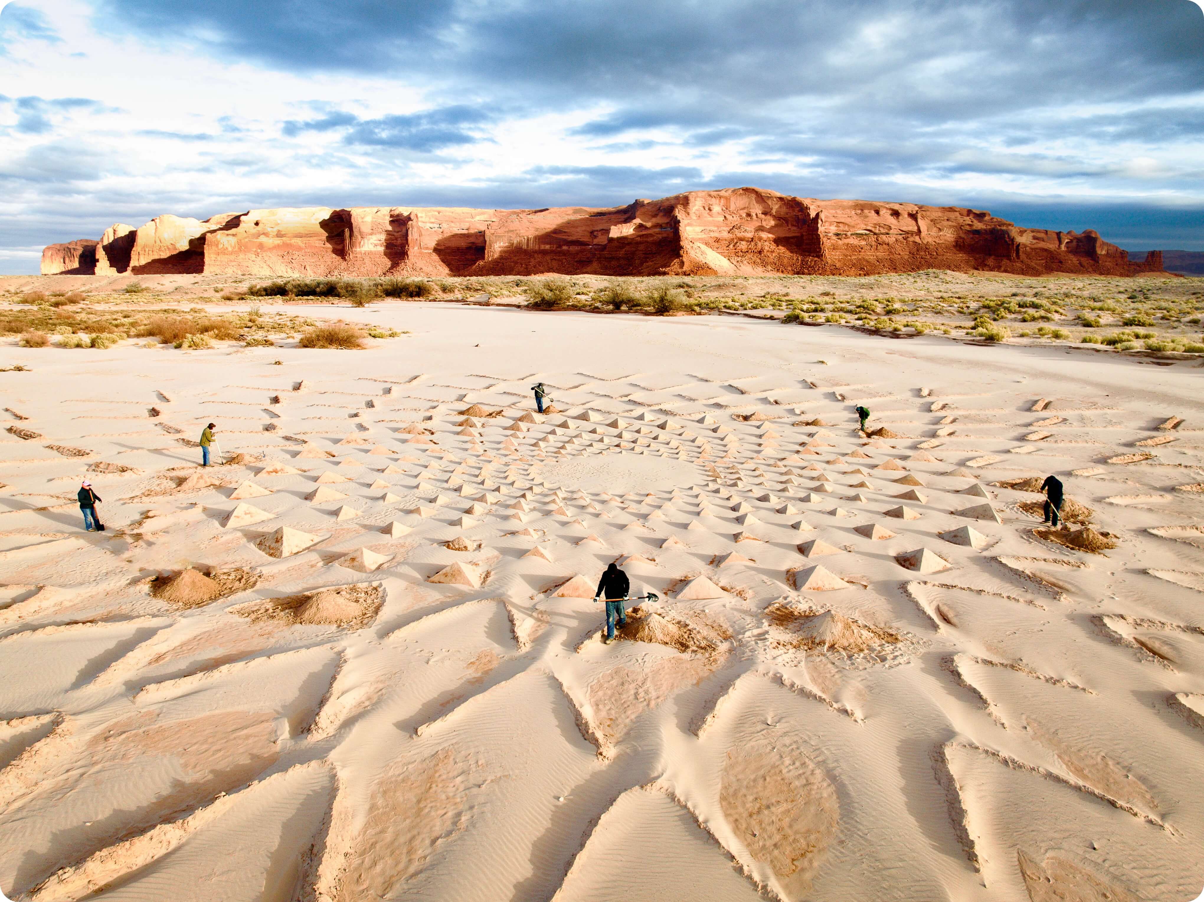 A group of people digging in the sand to build a massive piece of land art in a riverbed in front of Arizona red rocks