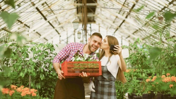Mariana and Tiago take a selfie in the greenhouse, he holds a tray of seedlings while she kisses him on the cheek.