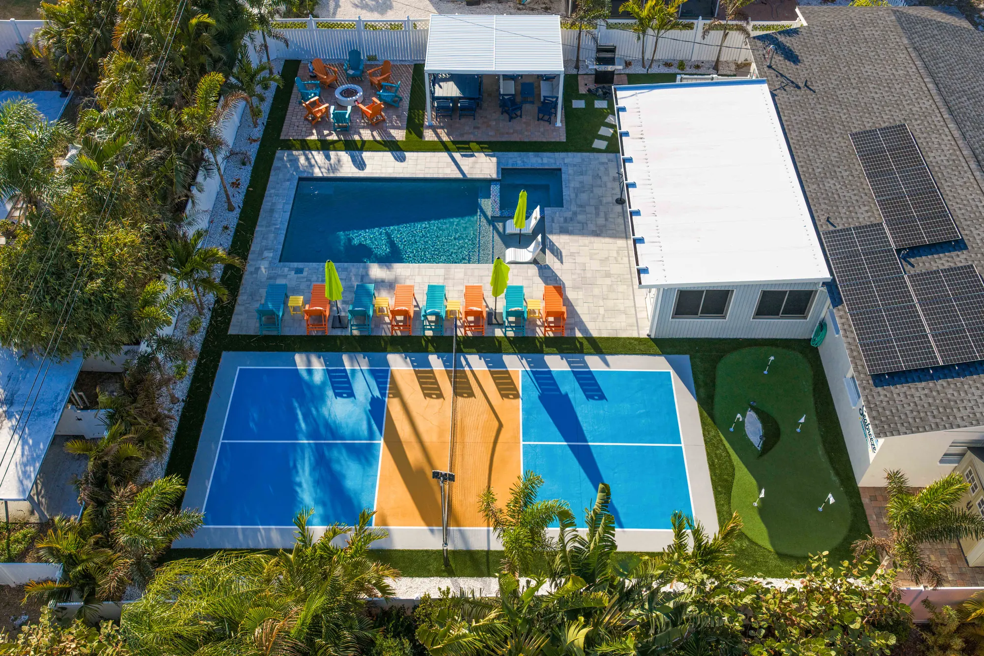 Aerial view of the backyard with the pool, a turquoise and marigold pickleball court, a putting green and a covered pavilion at Pickleball Resort, Bradenton, Florida