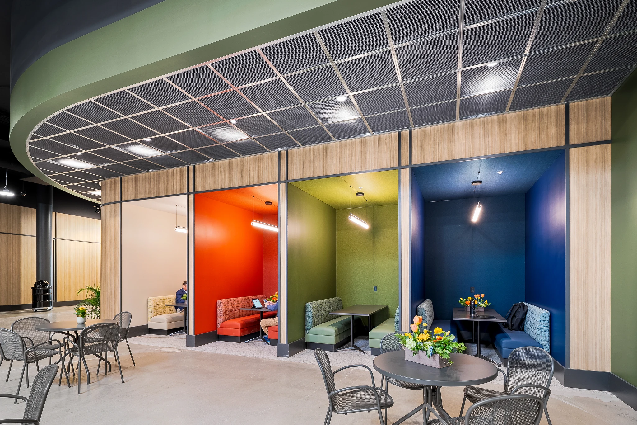 Crossroads seating alcoves in orange, green and blue beside cafe tables under a curved ceiling