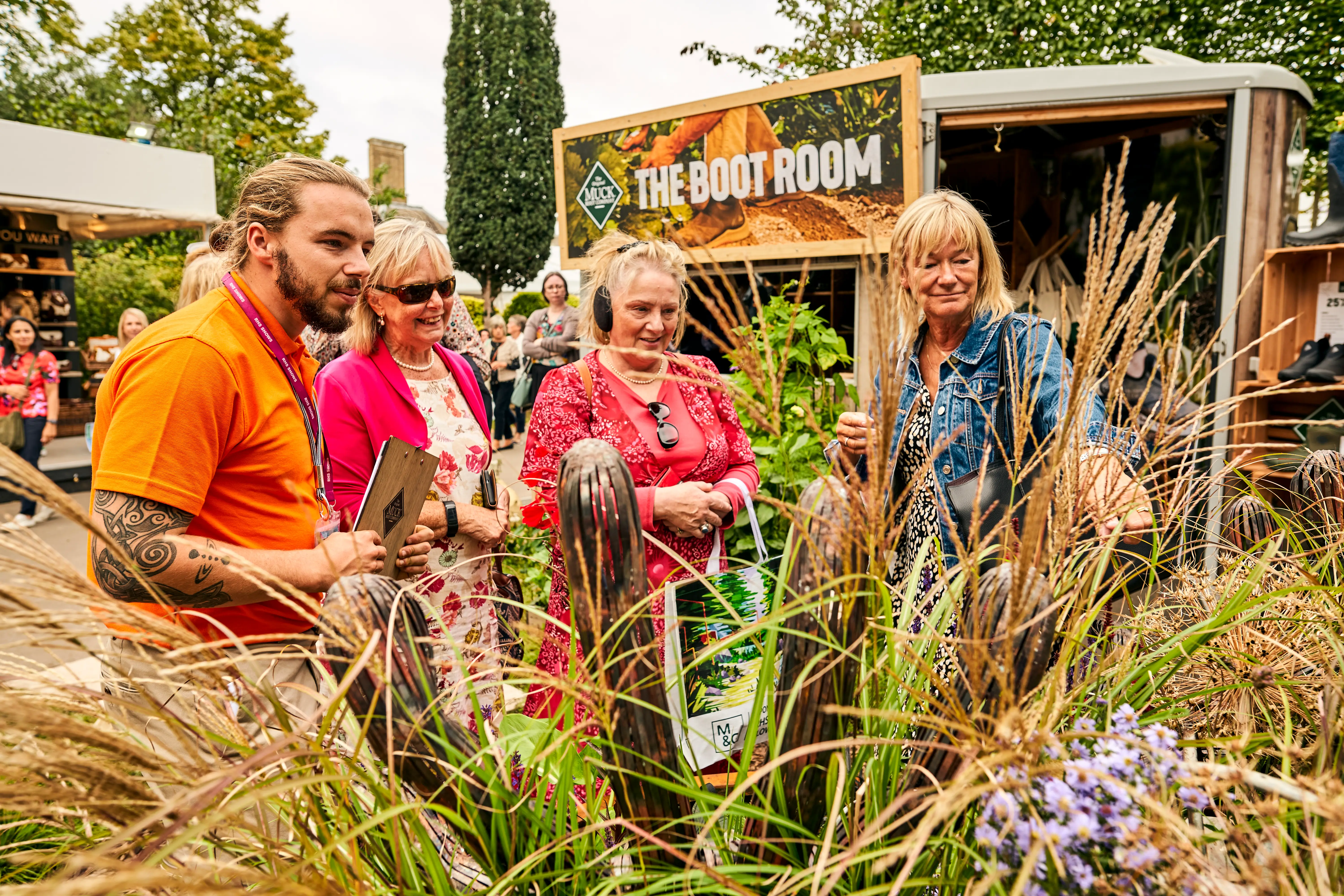 Four people gather around plants in a garden, chatting and enjoying the natural surroundings.