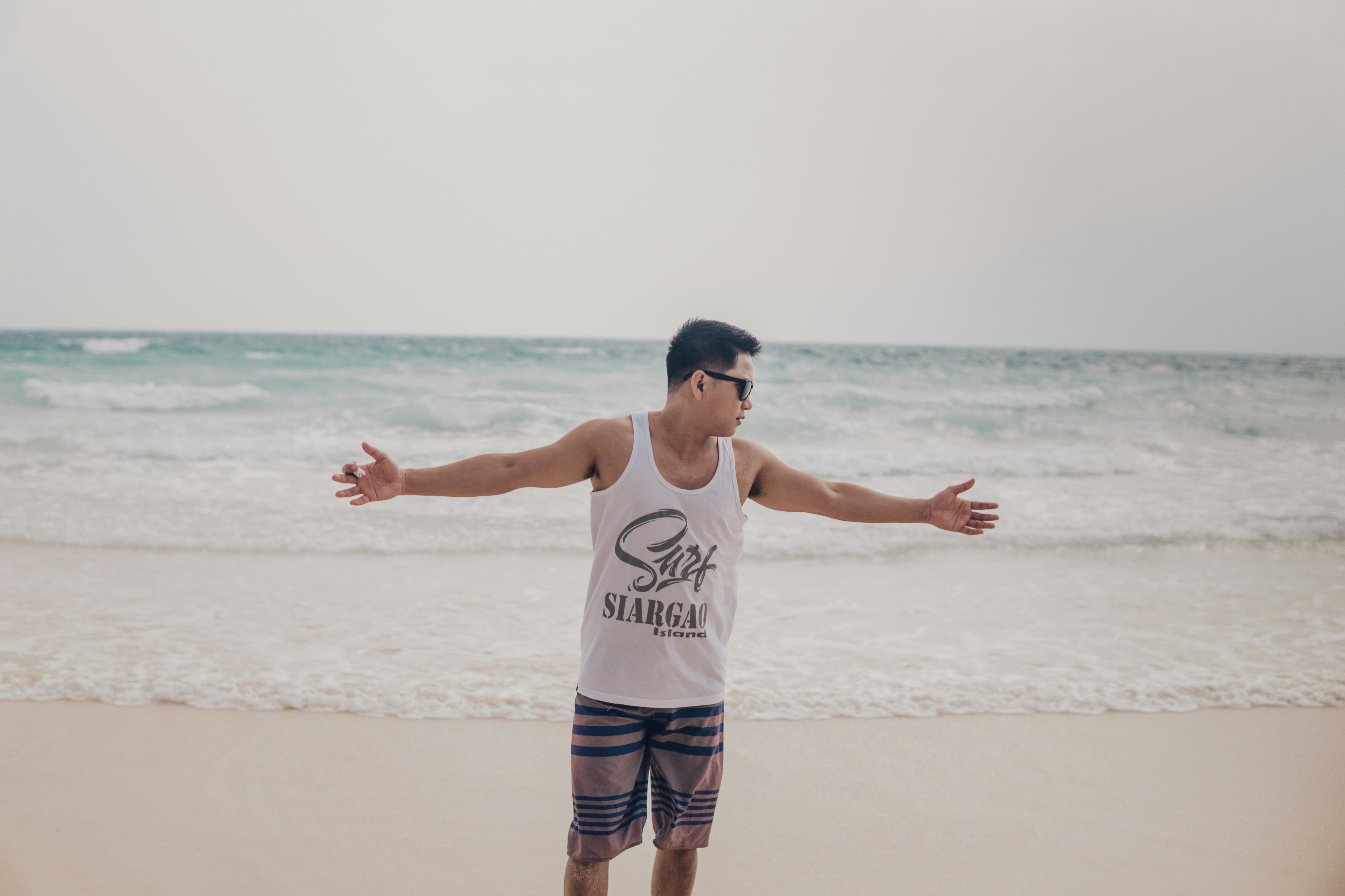 man in white crew neck t-shirt and blue shorts standing on beach during daytime