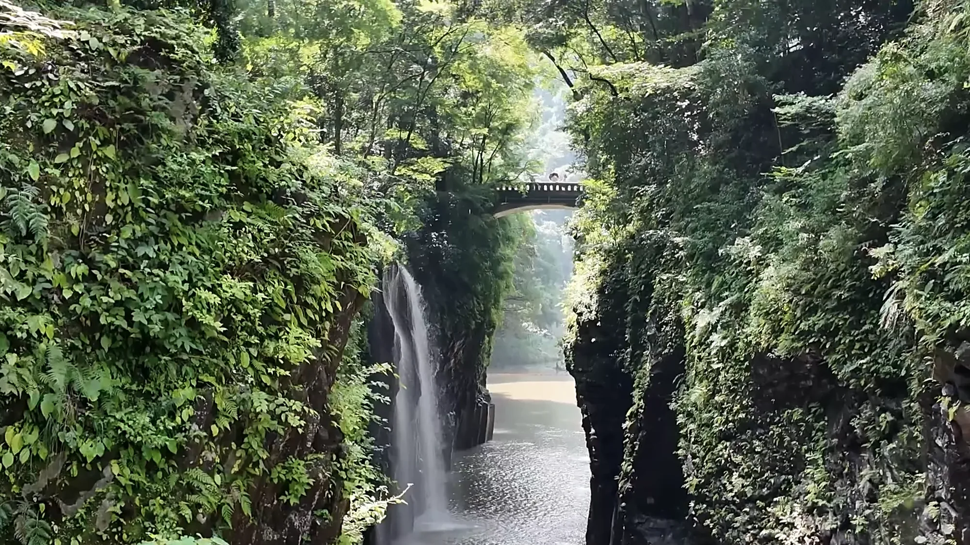 A tall waterfall in a mossy gorge near Kurokawa Onsen, a footbridge crossing above