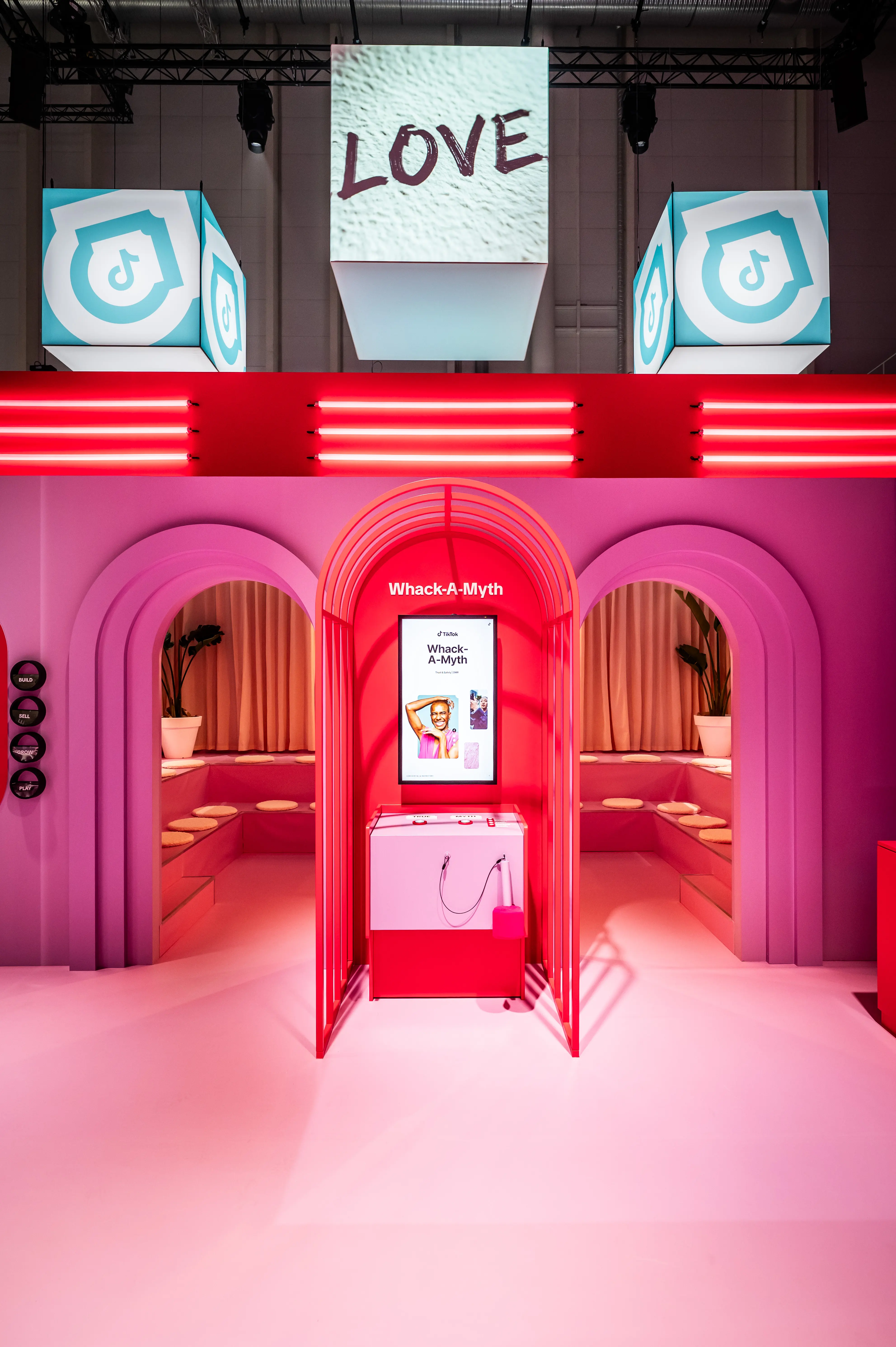 Whack-A-Myth game arch in the pink booth with neon strip, LOVE cube and TikTok shield cubes above.