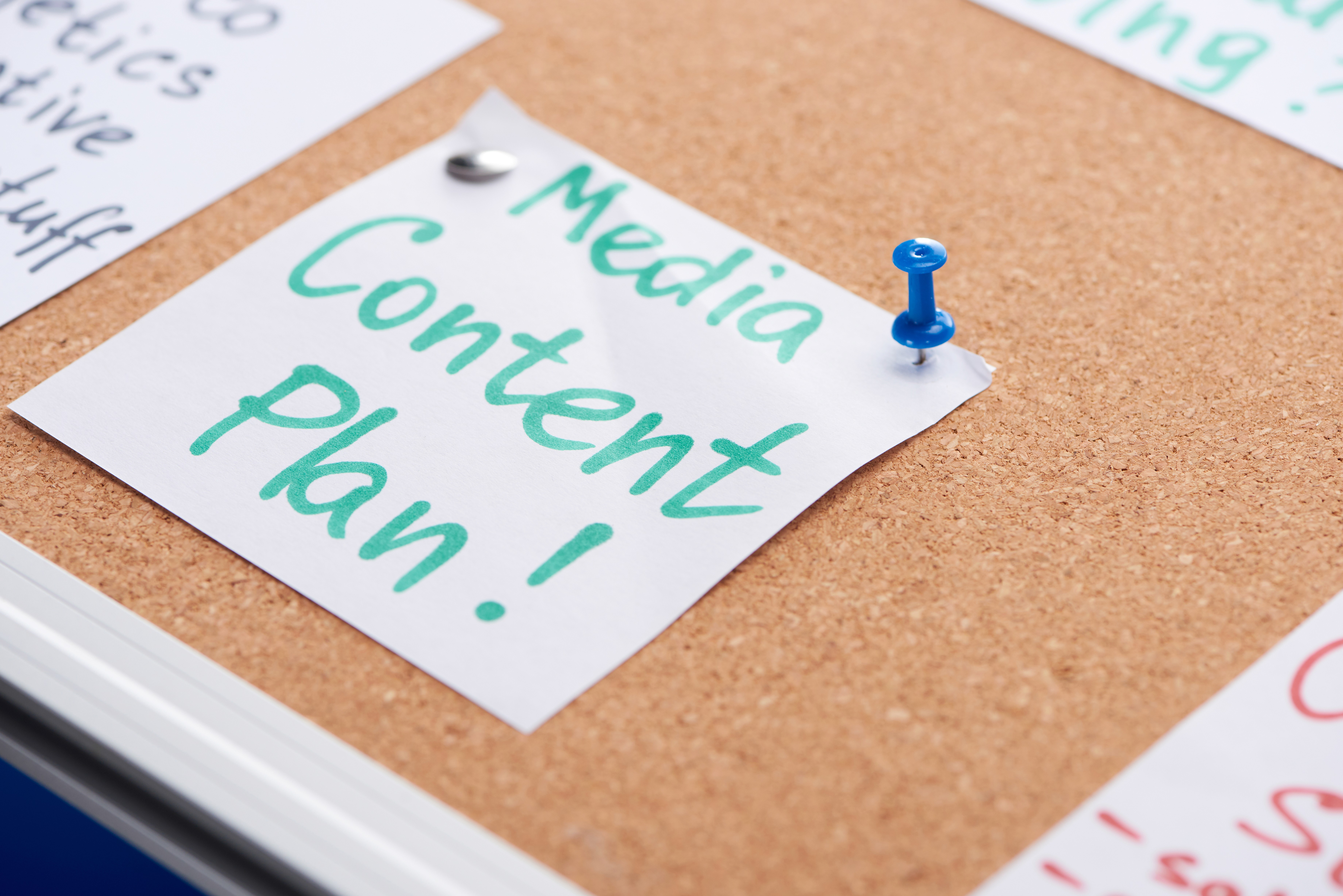 A handwritten Media Content Plan note pinned to a corkboard surrounded by other planning notes, representing the structured content planning system that makes consistent video production manageable for service business founders