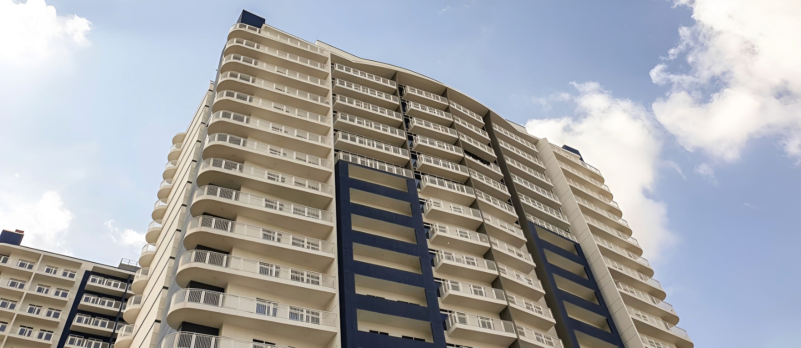 Low-angle architectural view of Geepas Tower's modern facade and balconies under a bright sky.