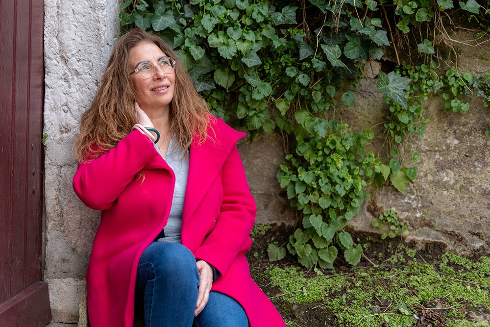 Portrait femme assise contre un mur avec végétation