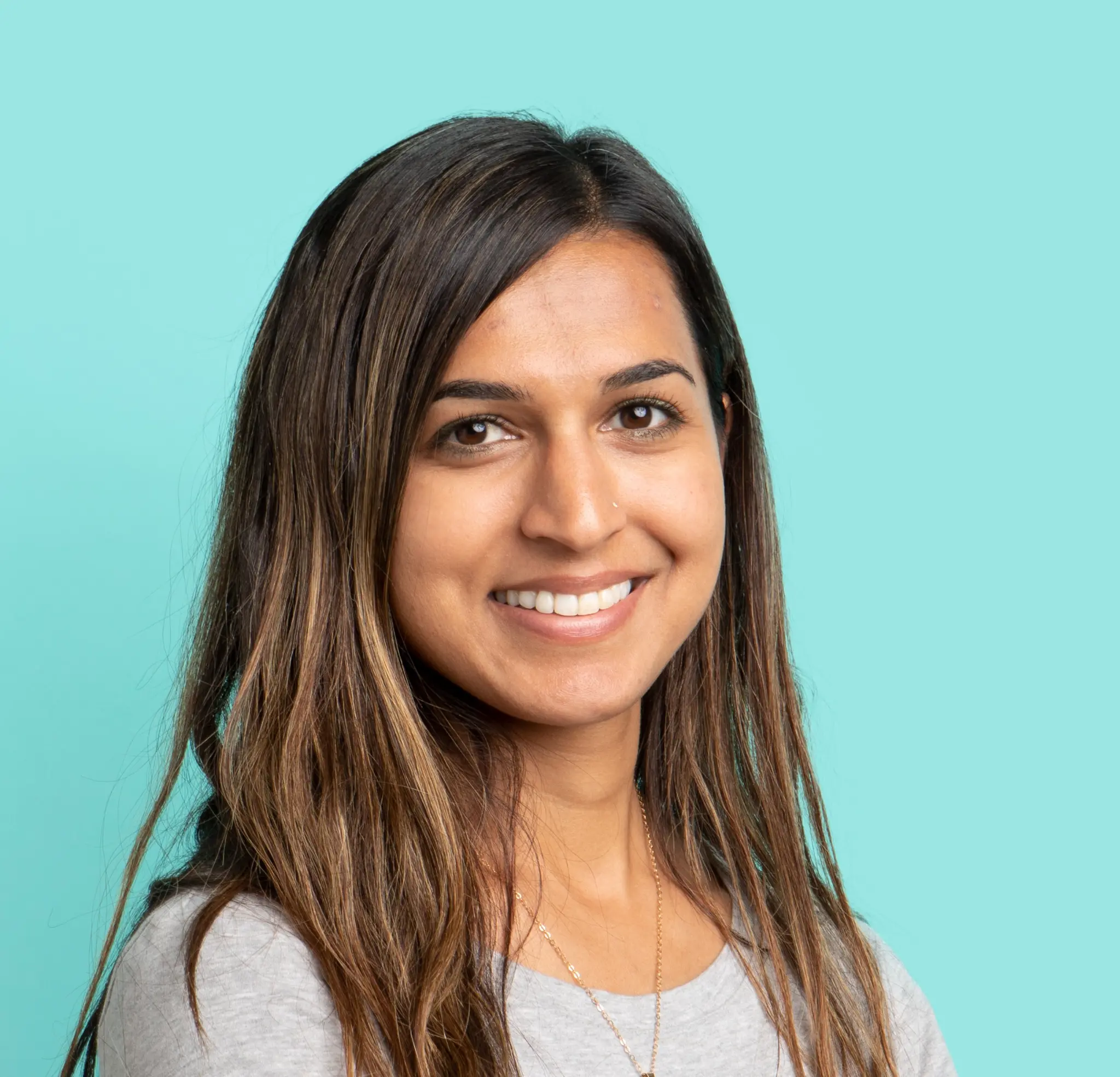 Woman with long brown hair smiling on blue background.