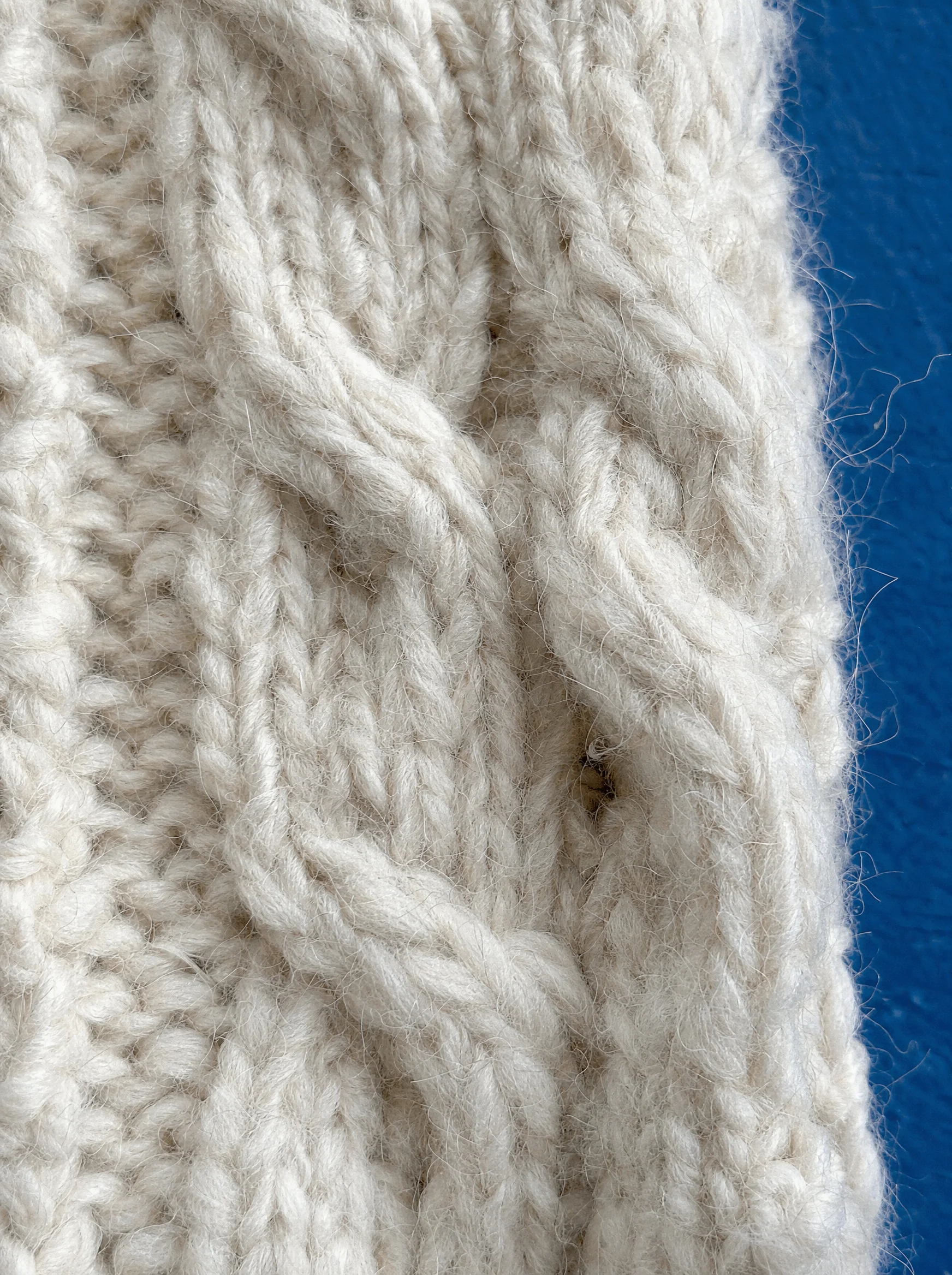 Close-up of undyed cream cable knit against cobalt blue