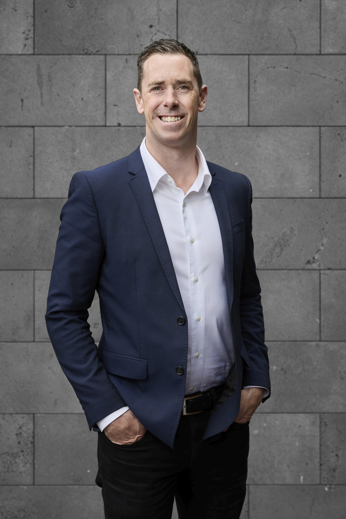 A portrait of Nick Maxwell, wearing a navy blazer, smiling.