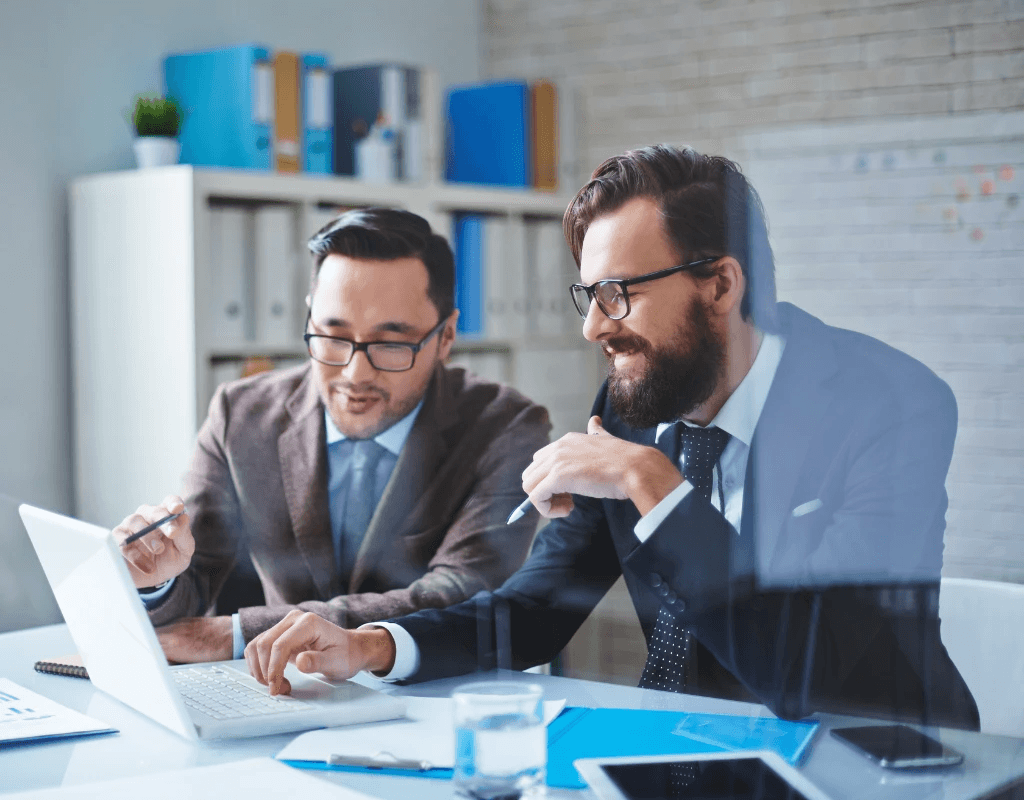 Two businessmen discussing over a laptop in a modern office setting.