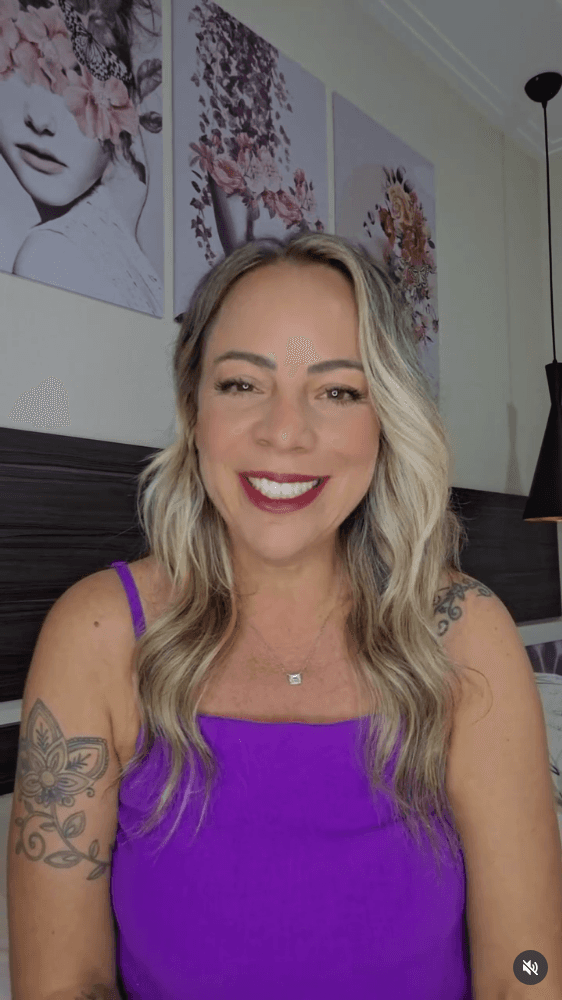 Smiling female therapist with short gray hair, wearing a brown top and a purple shawl, surrounded by a cozy background.
