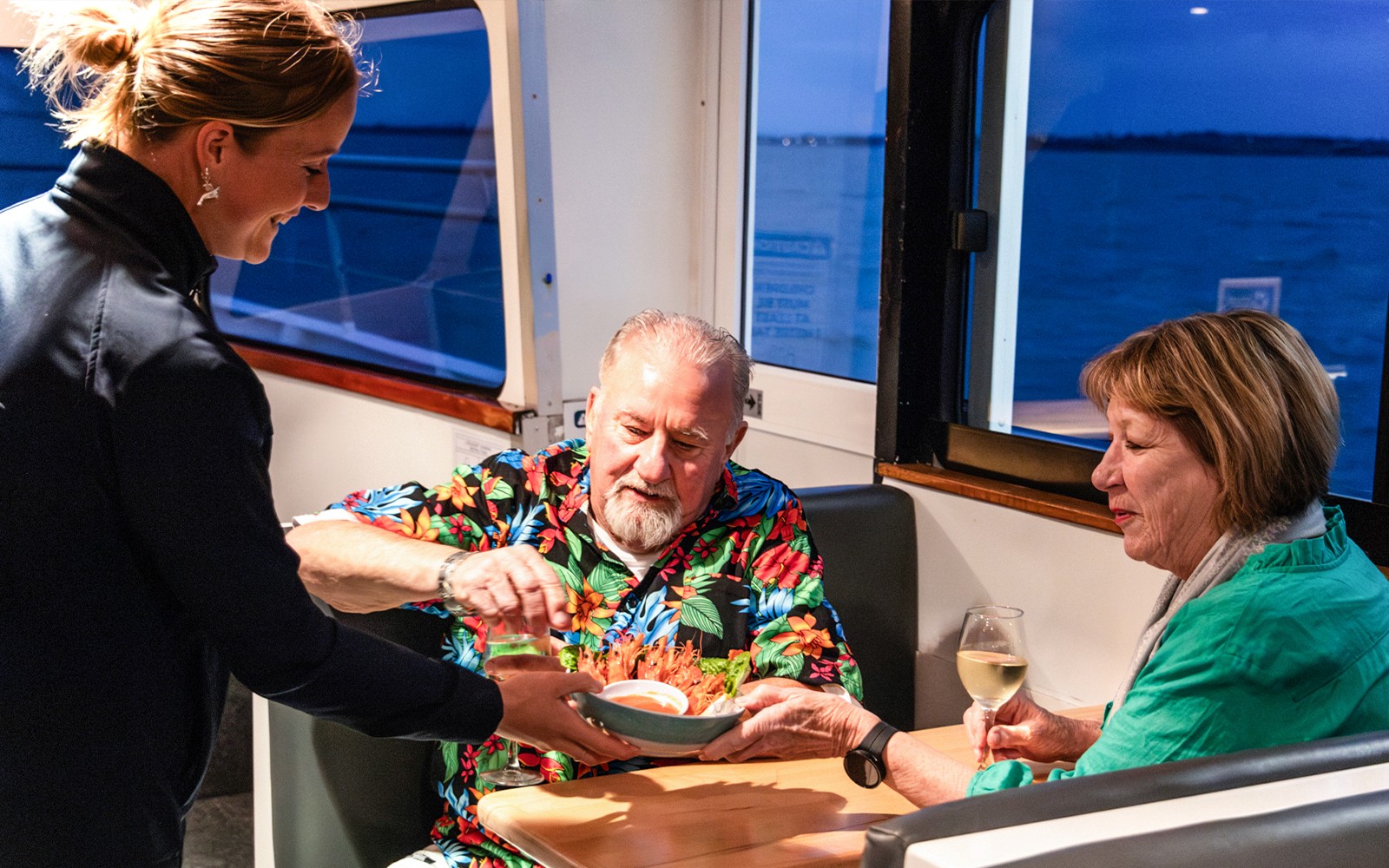 Il cameriere offre un piatto di frutti di mare a una coppia durante una crociera al tramonto a Phillip Island.