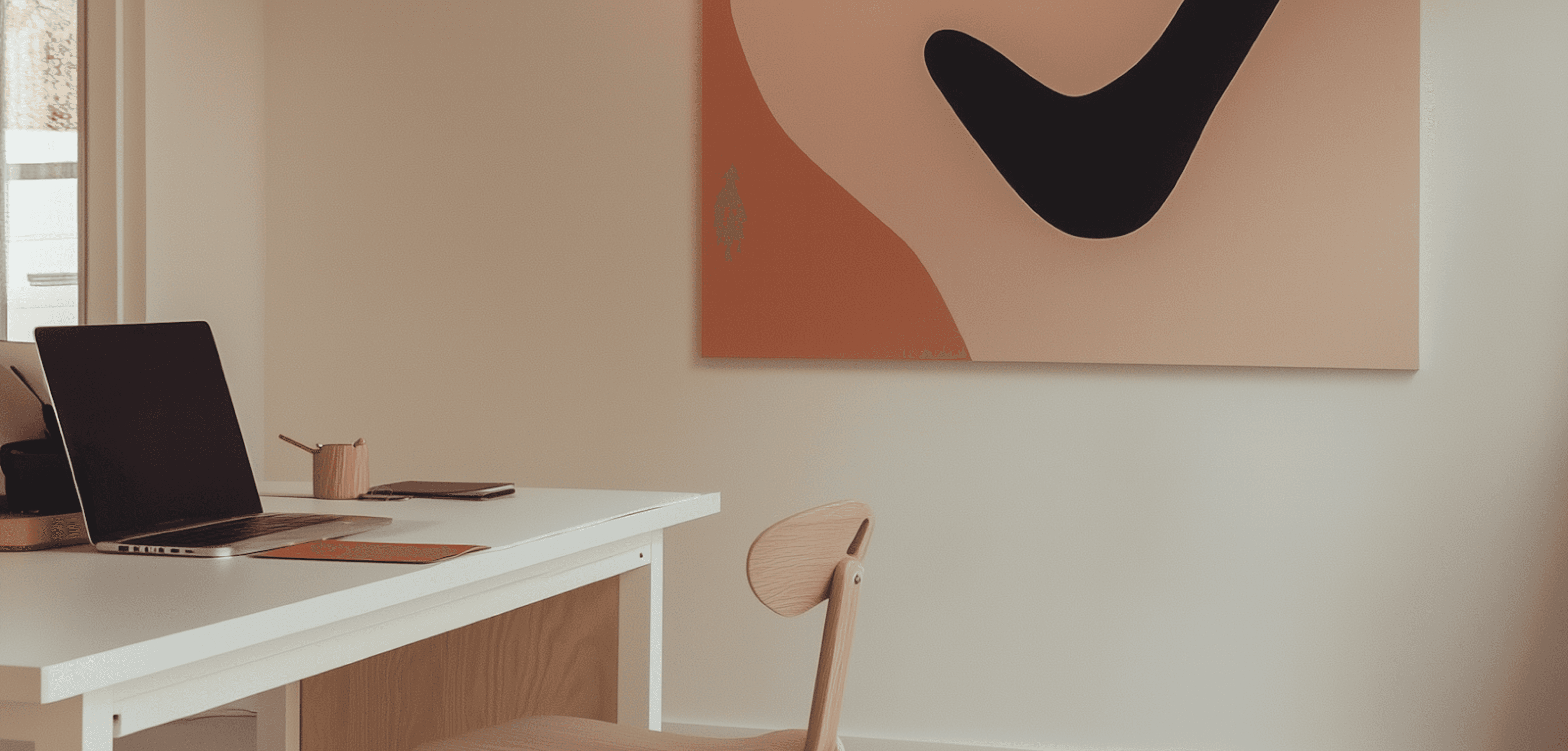 Minimalist desk setup with a laptop, phone, and abstract wall art in a bright workspace
