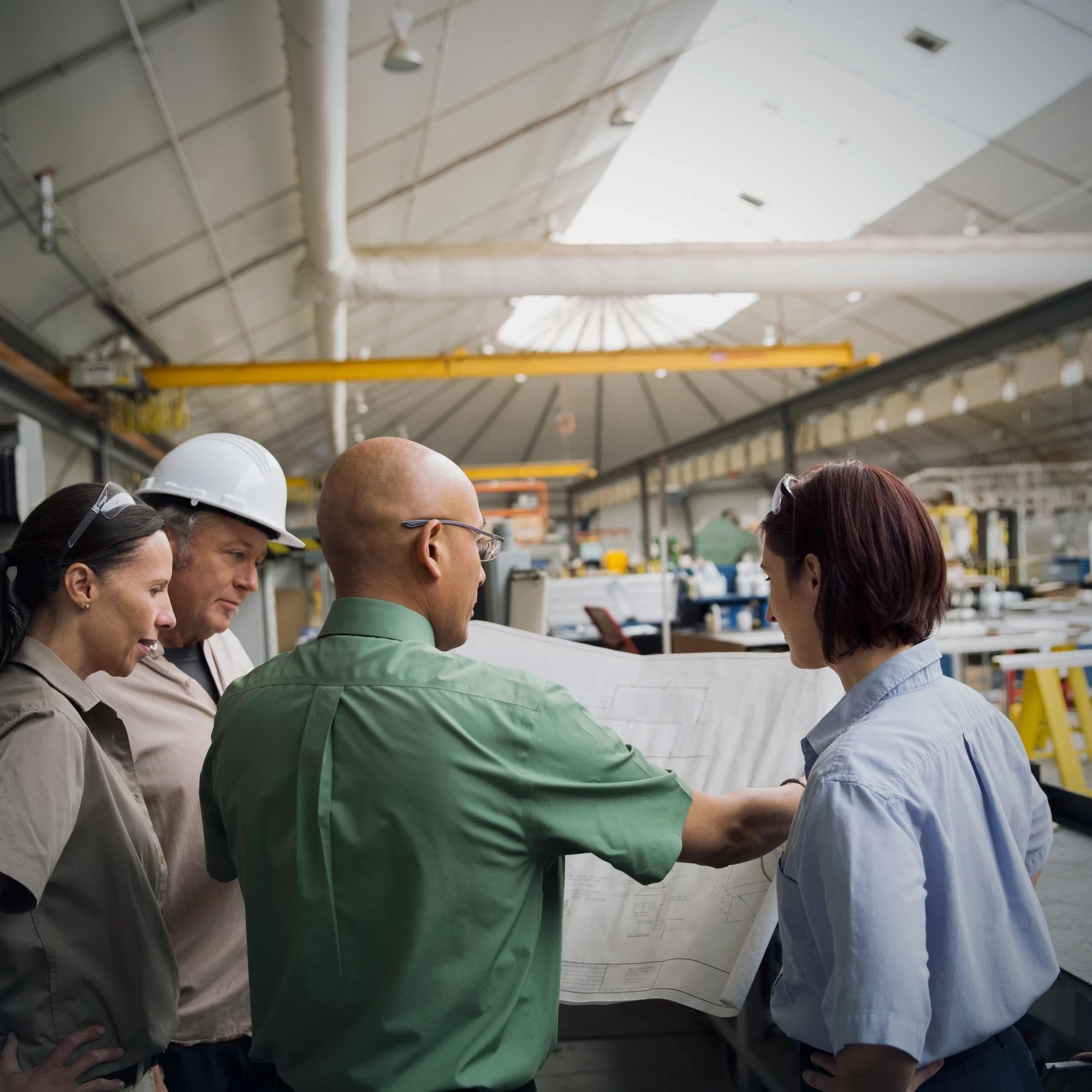 Plant team in hard hats gathered around a drawing on the floor, working through it together