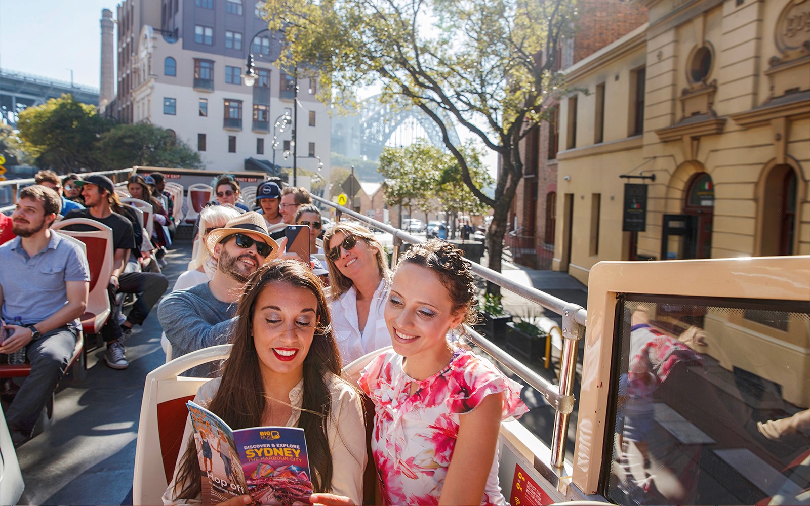 Passengers enjoying a sunny ride on Big Bus Sydney with cityscape views.