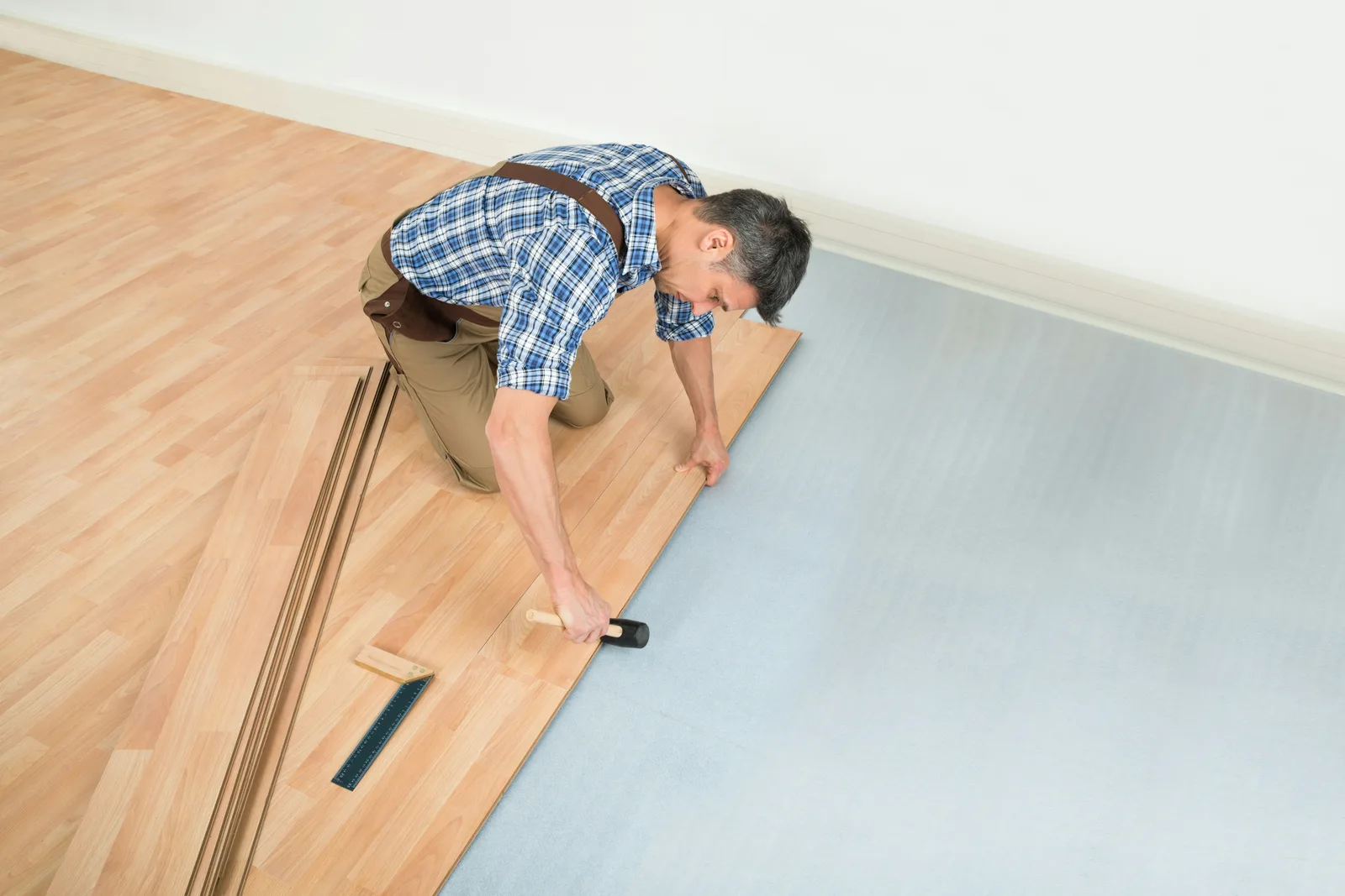 Worker fitting laminate planks on blue underlayment from overhead view