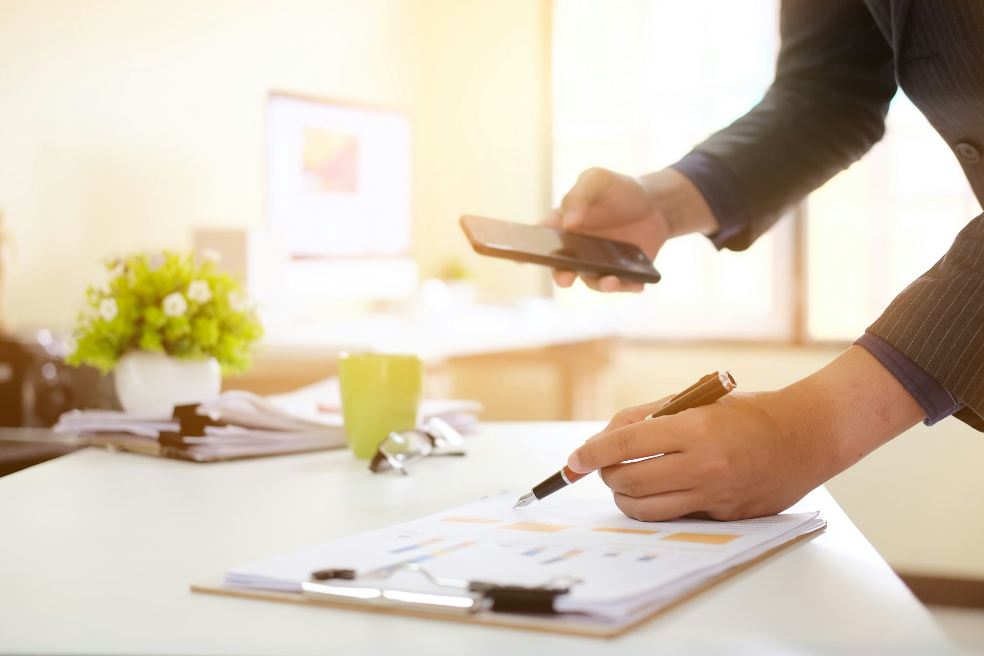 A person holding a phone while writing on a paper