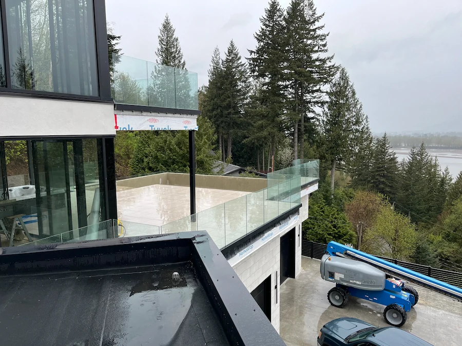 Frameless glass railing installed on an elevated patio of a modern home, overlooking tall evergreens in a forested BC landscape.