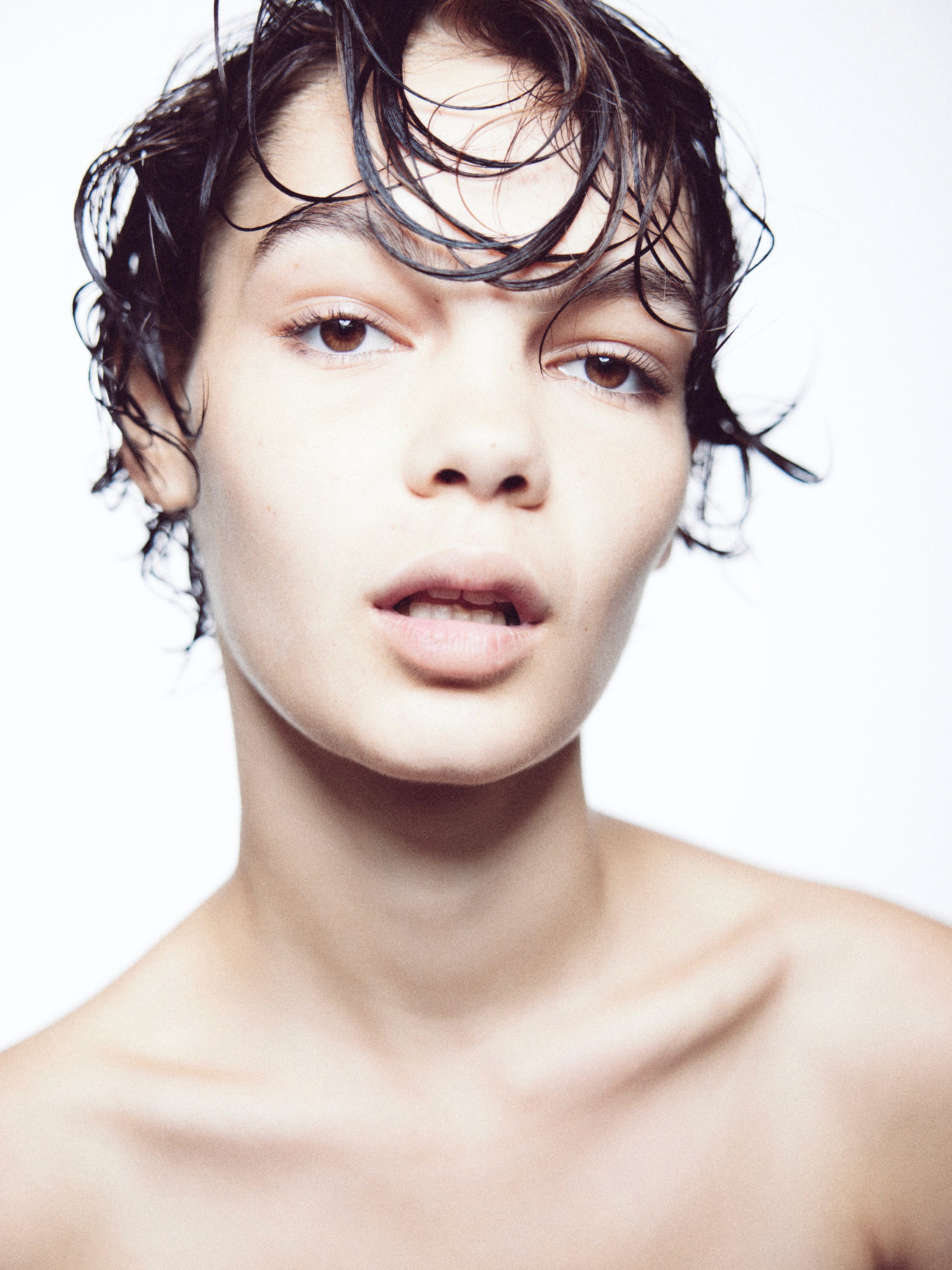 A beauty portrait on a white background of a model with damp messy hair, looking at camera with bare shoulders and her mouth open slightly.