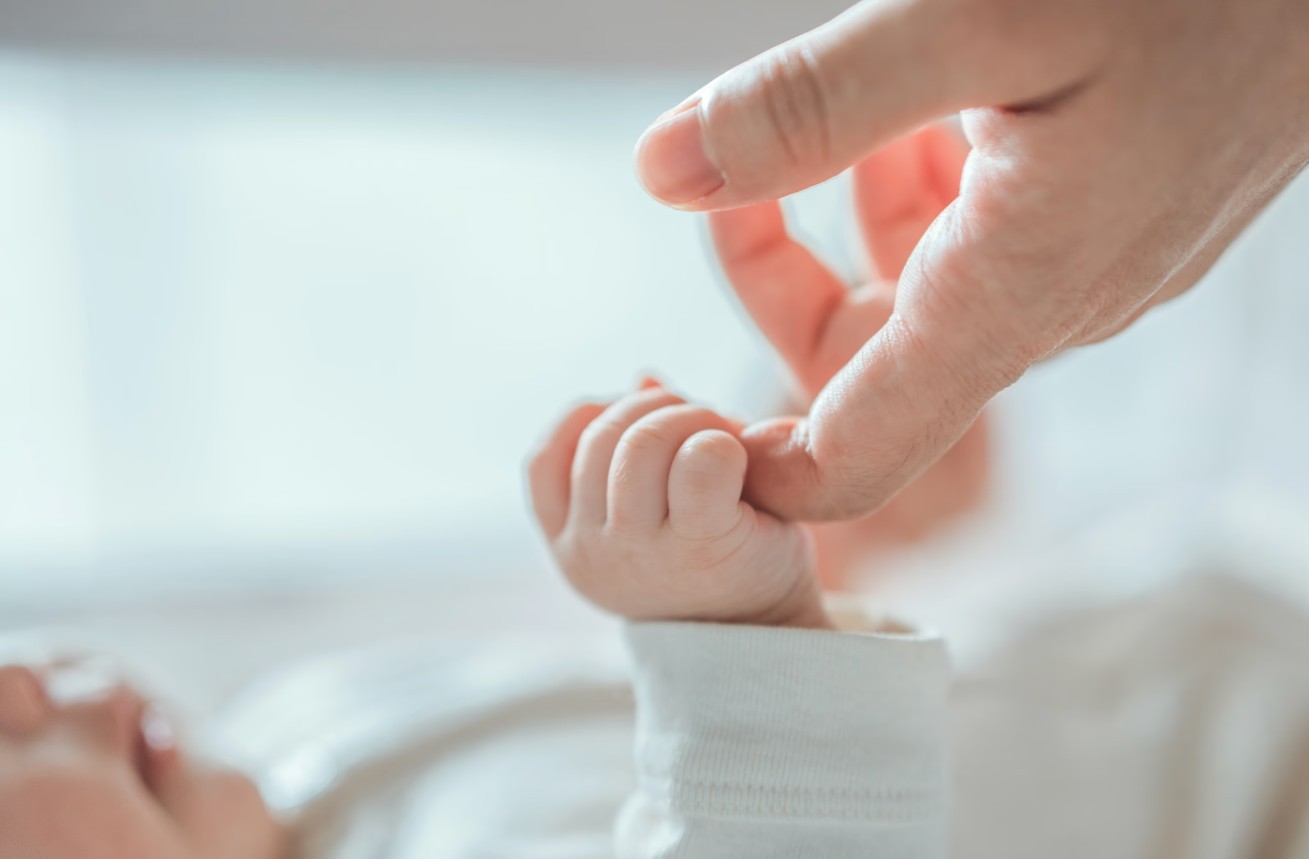 Newborn hospital photo showing a baby's little fingers wrapped around a paren'ts finger.