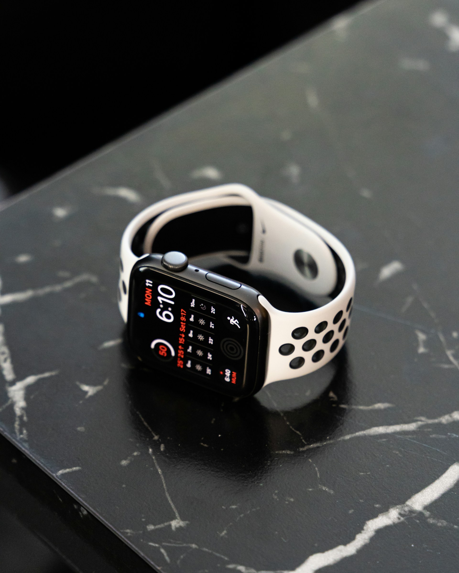 Close-up of an Apple Watch with a white and black sport band resting on a black marble surface.