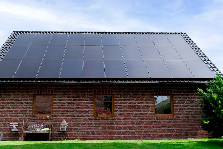 Ziegelfassade mit Solarmodulen auf dem Dach und zwei Fenstern.
