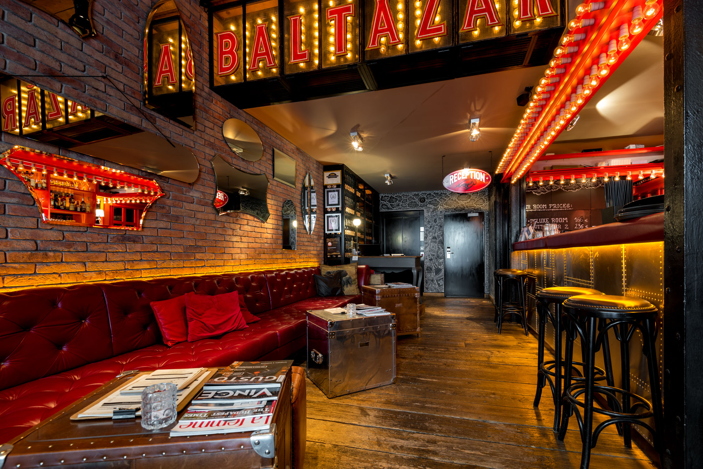 A dimly lit bar interior with red leather booths, neon signs, and a long wooden counter lined with tall stools.